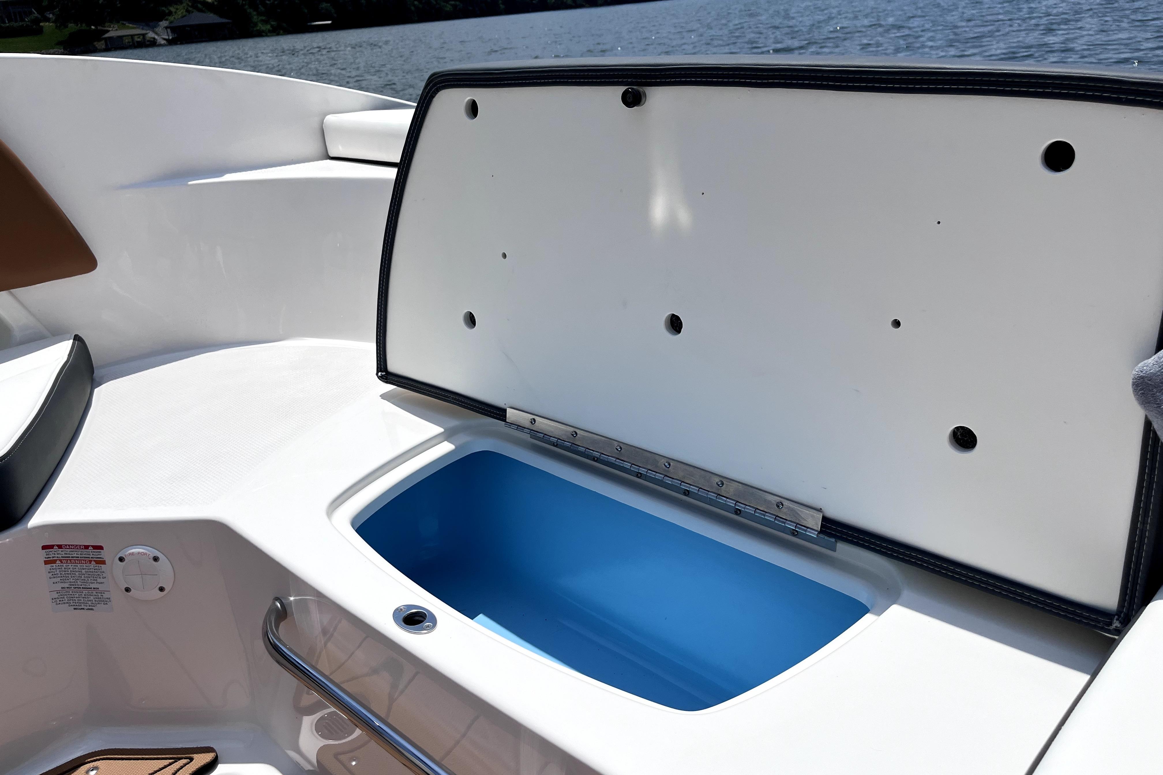 Open storage compartment on 2025 Chaparral 230 SSi boat, with blue interior, near water.