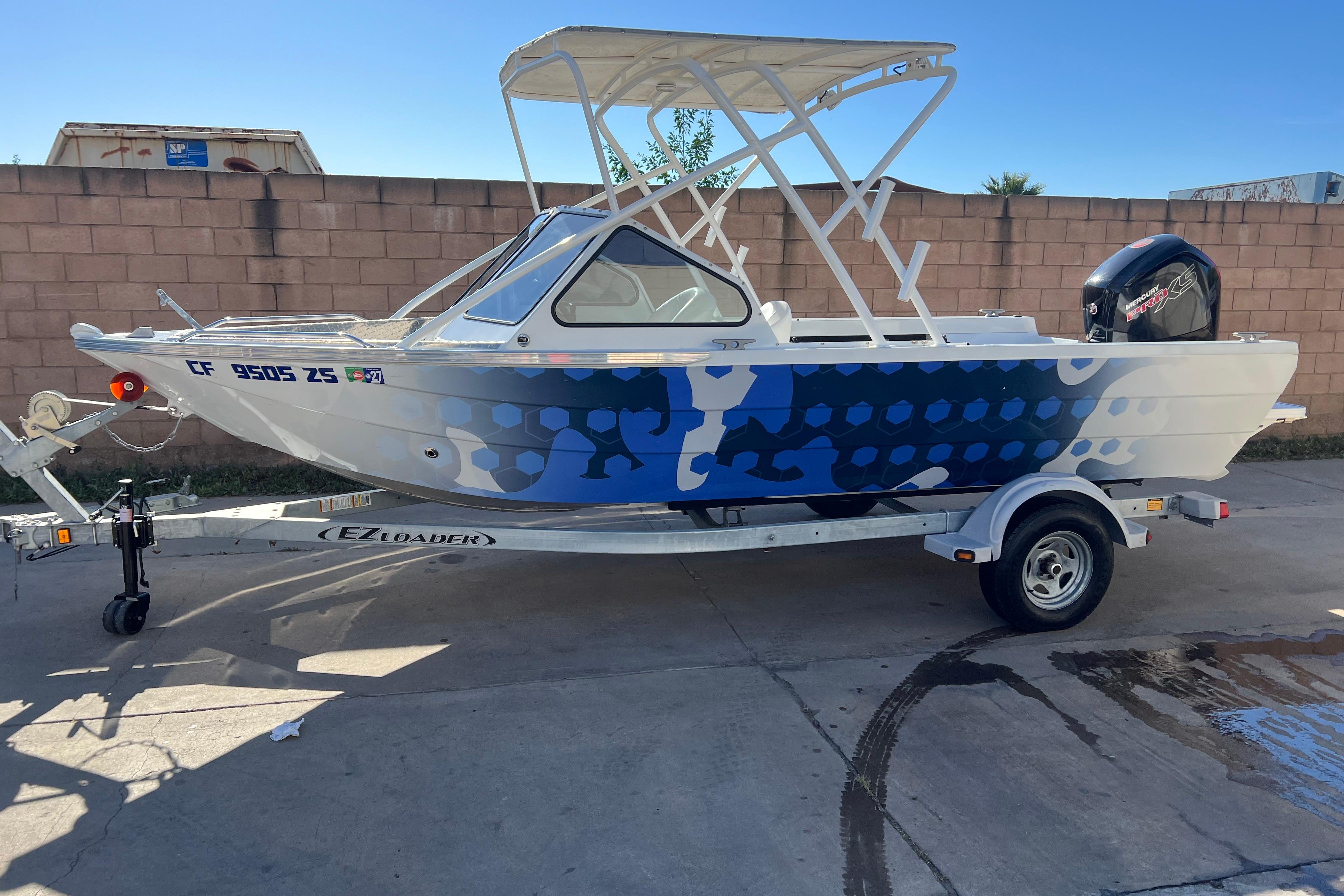 2019 KingFisher 1825 Falcon boat on trailer, blue camo design, parked outdoors.