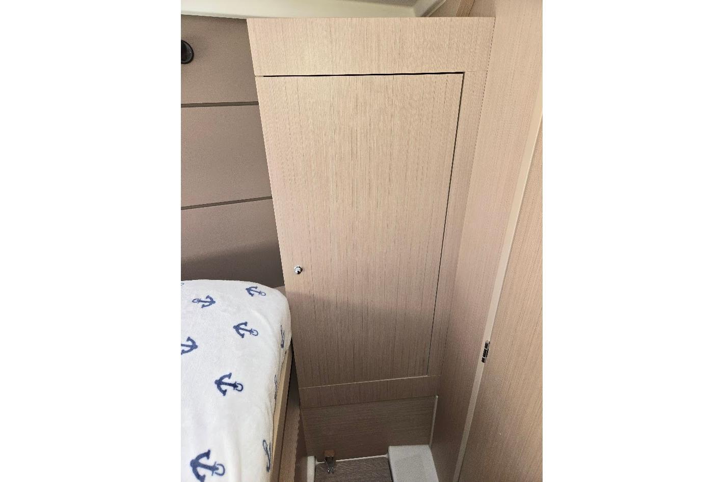 Interior cabin of 2023 Beneteau Oceanis 38.1 yacht with wooden paneling and anchor-patterned bedding.