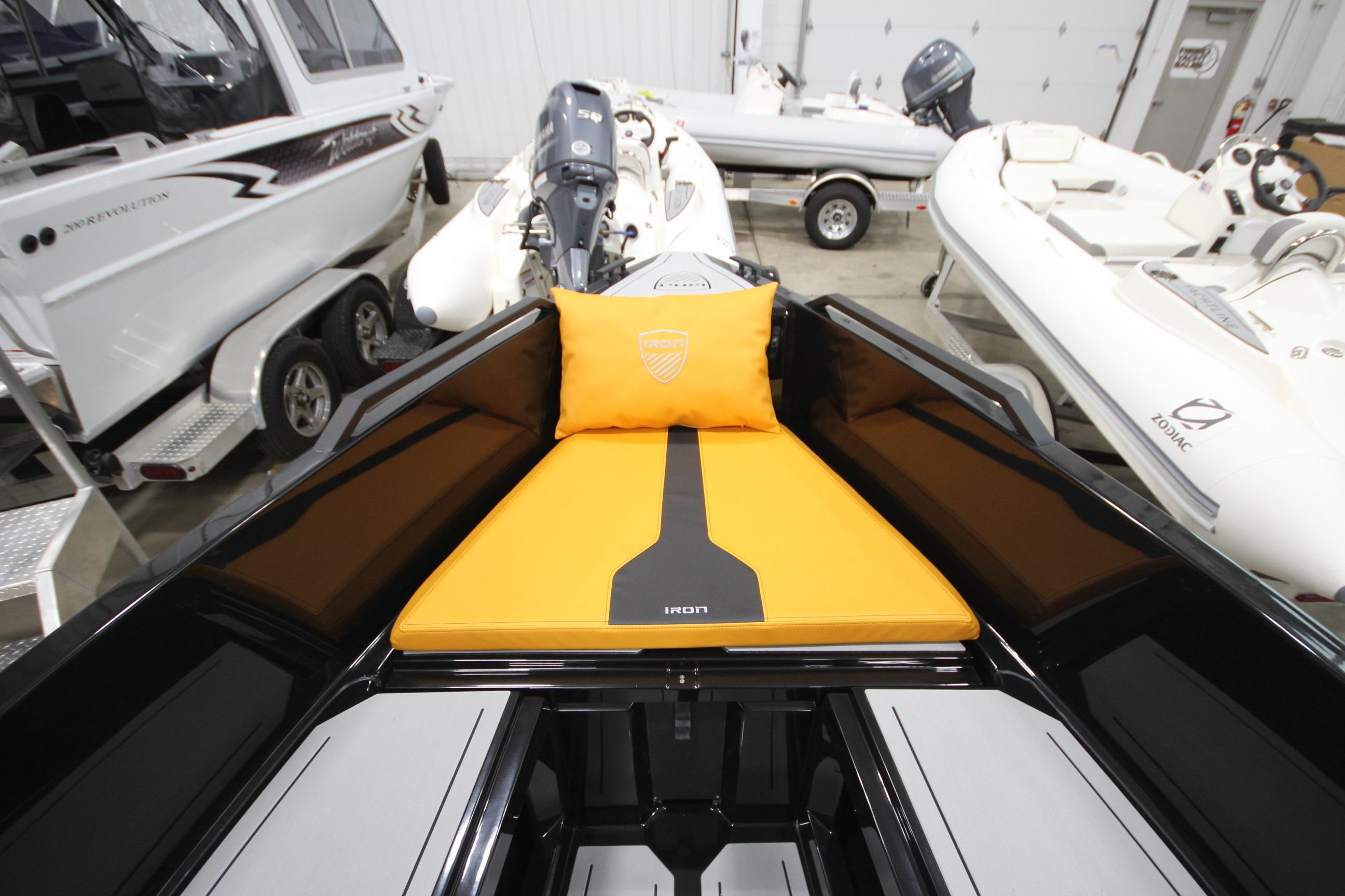 Modern Iron 767 boat interior with orange cushion, sleek design, and adjacent boats in showroom.