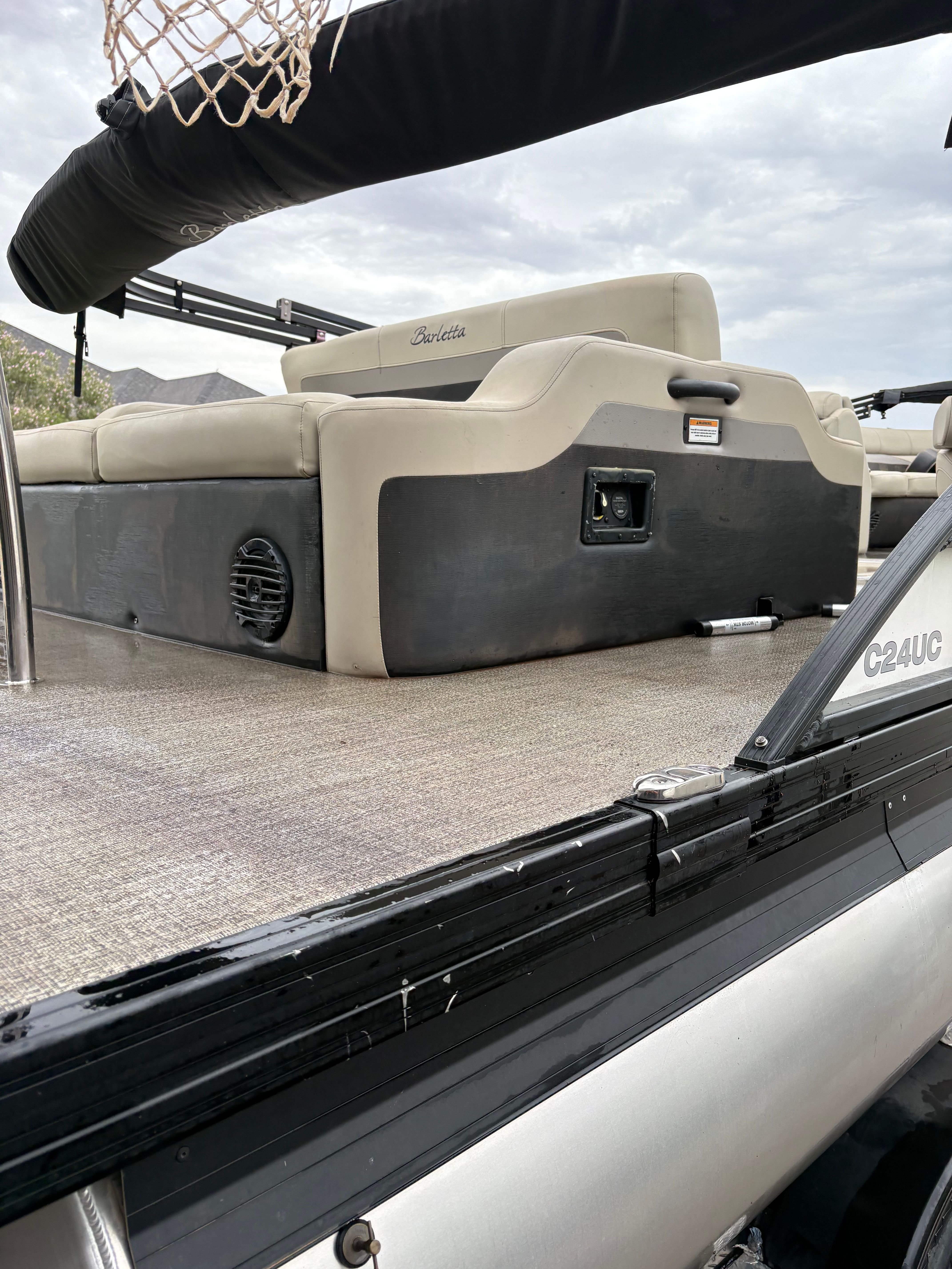 The image shows the rear of a Barletta C24UC pontoon boat with beige seats and black railing.