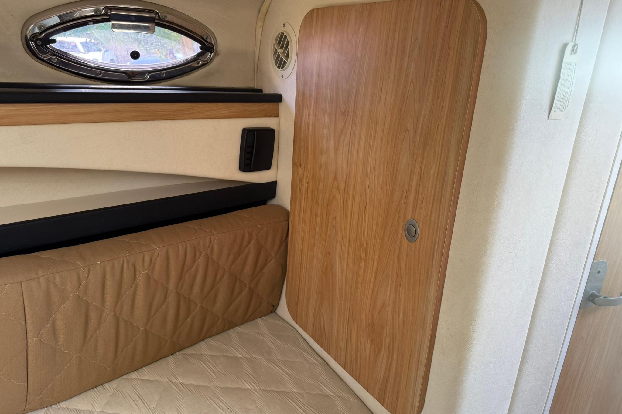Interior cabin of 2006 Sea Ray 270 Amberjack with wood paneling and porthole window.