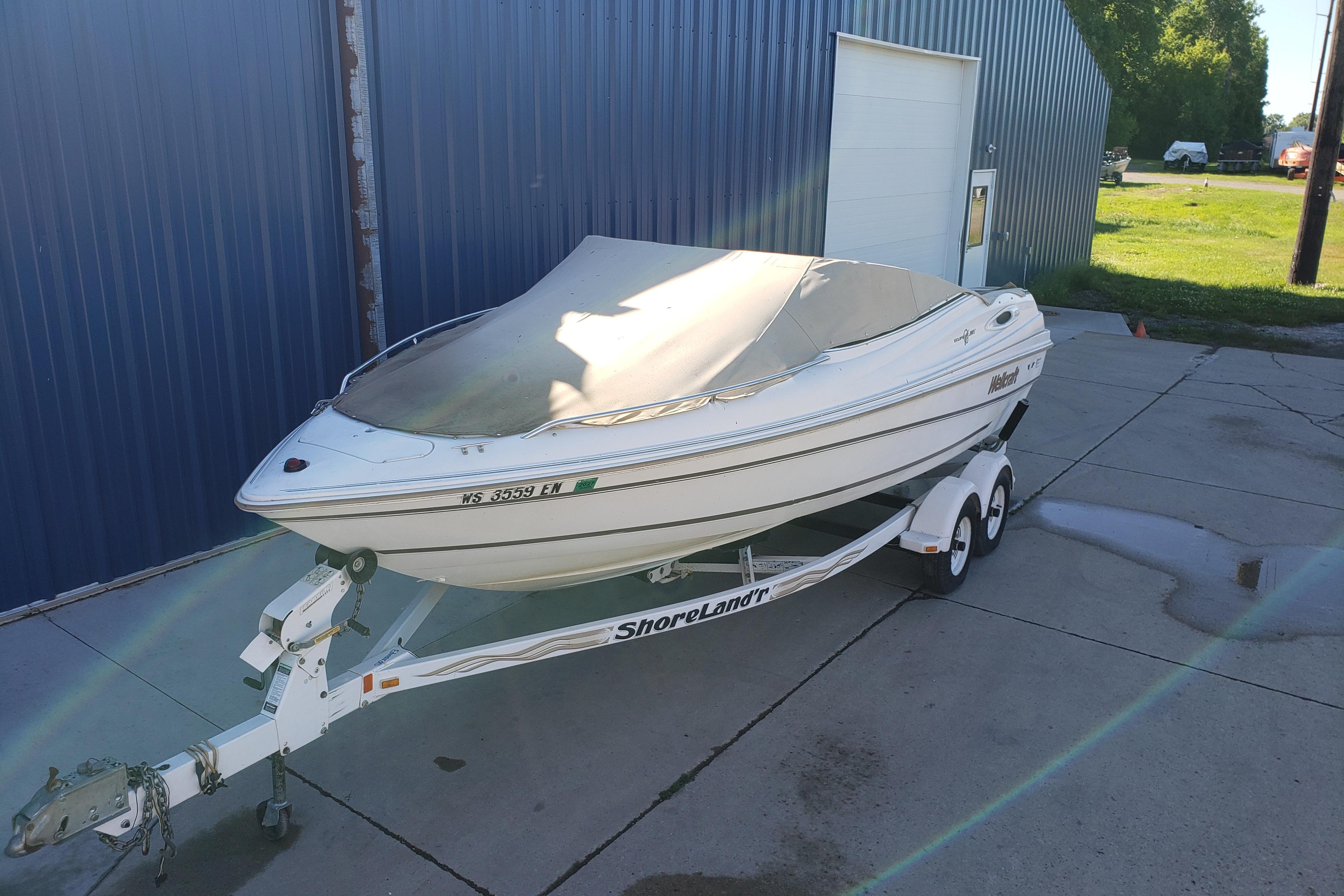1998 Wellcraft Eclipse 2000 SS boat on trailer, covered, parked by blue building.