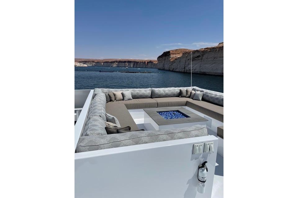 Luxurious yacht deck with plush seating and fire pit, overlooking serene waters and cliffs.