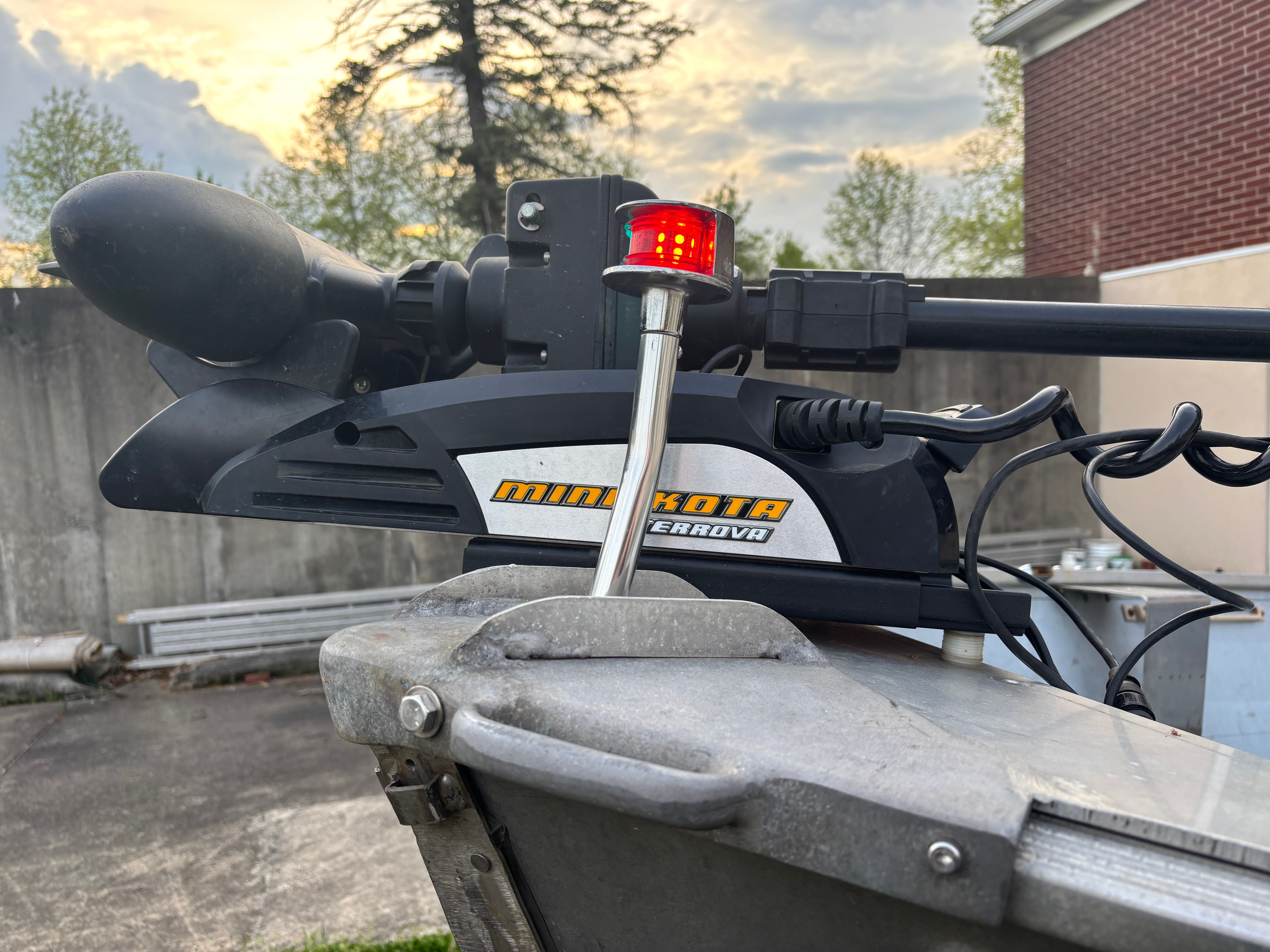 Close-up of a boat motor with a red light, trees and buildings in the background.