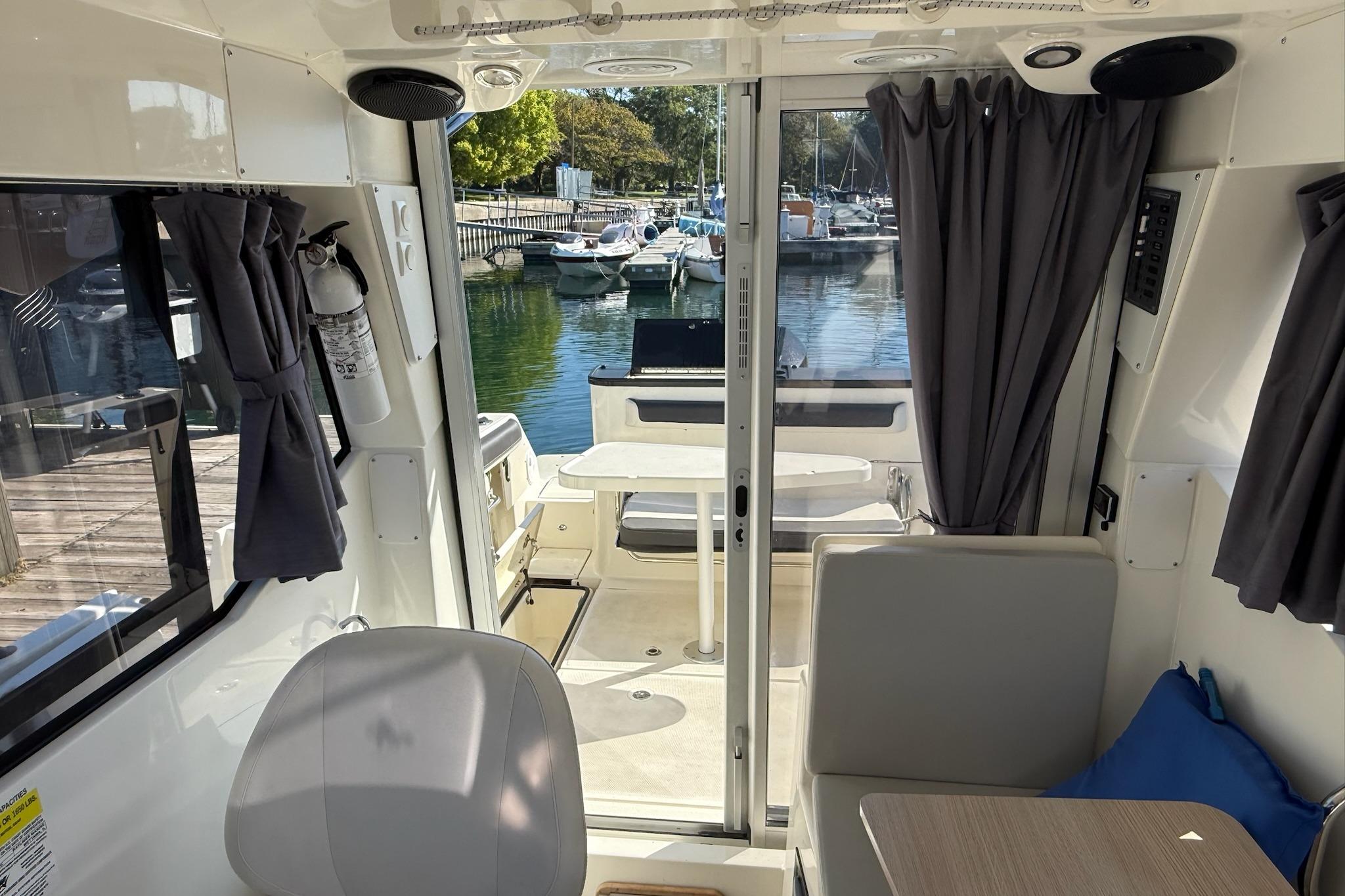 2024 Bayliner Trophy T25 Pilothouse interior with seating, table, and marina view.