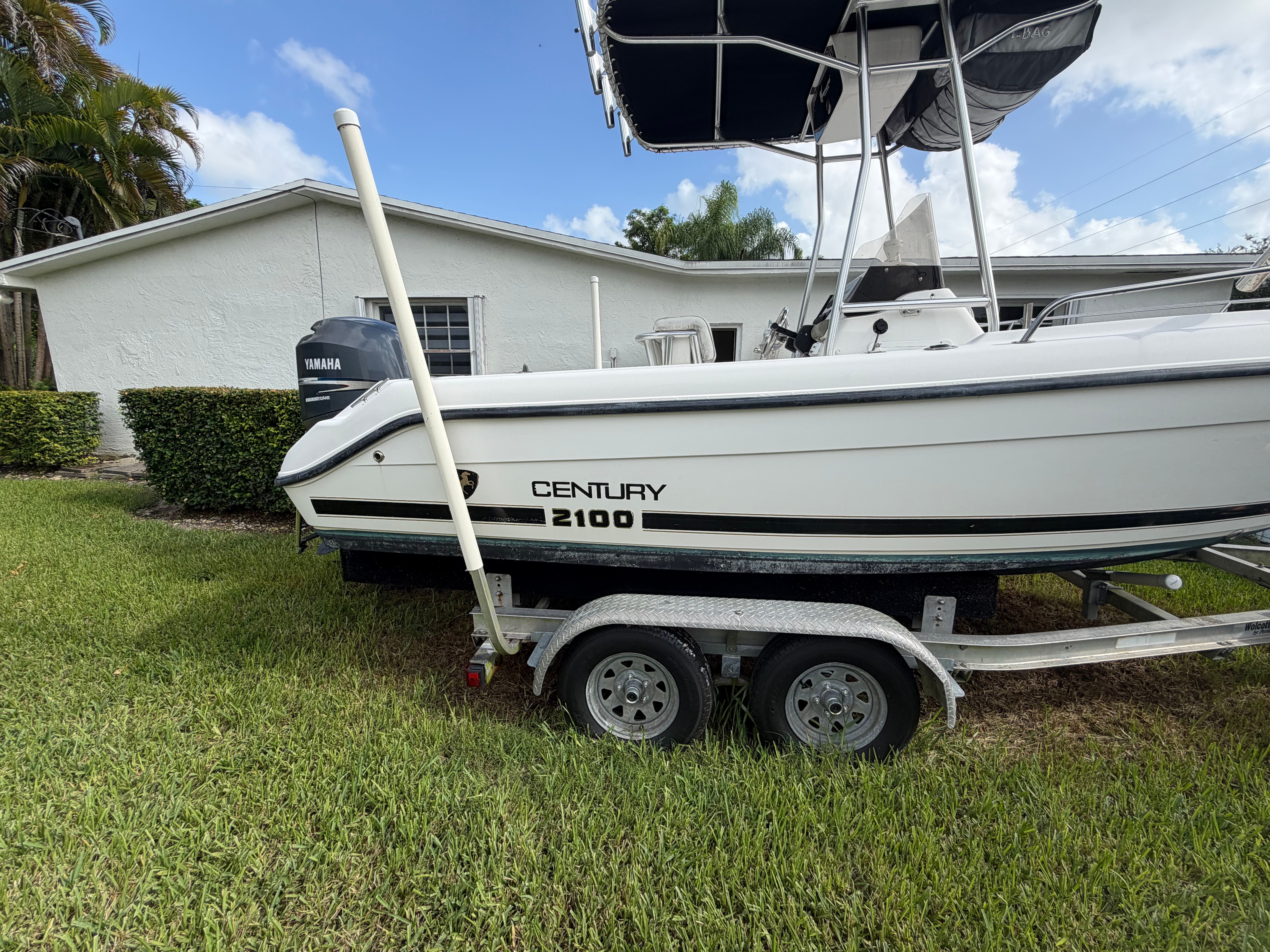 A 2001 Century 2100 Center Console boat on a trailer, parked on grass in front of a house.