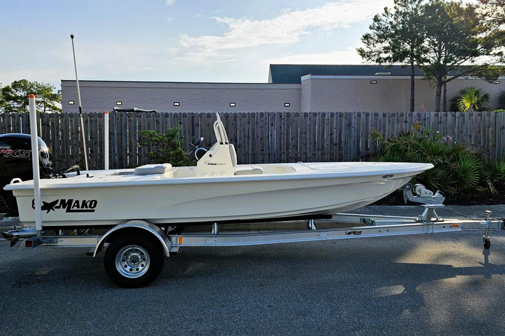 2026 Mako 18 Pro Skiff boat on trailer, parked outdoors near a wooden fence.