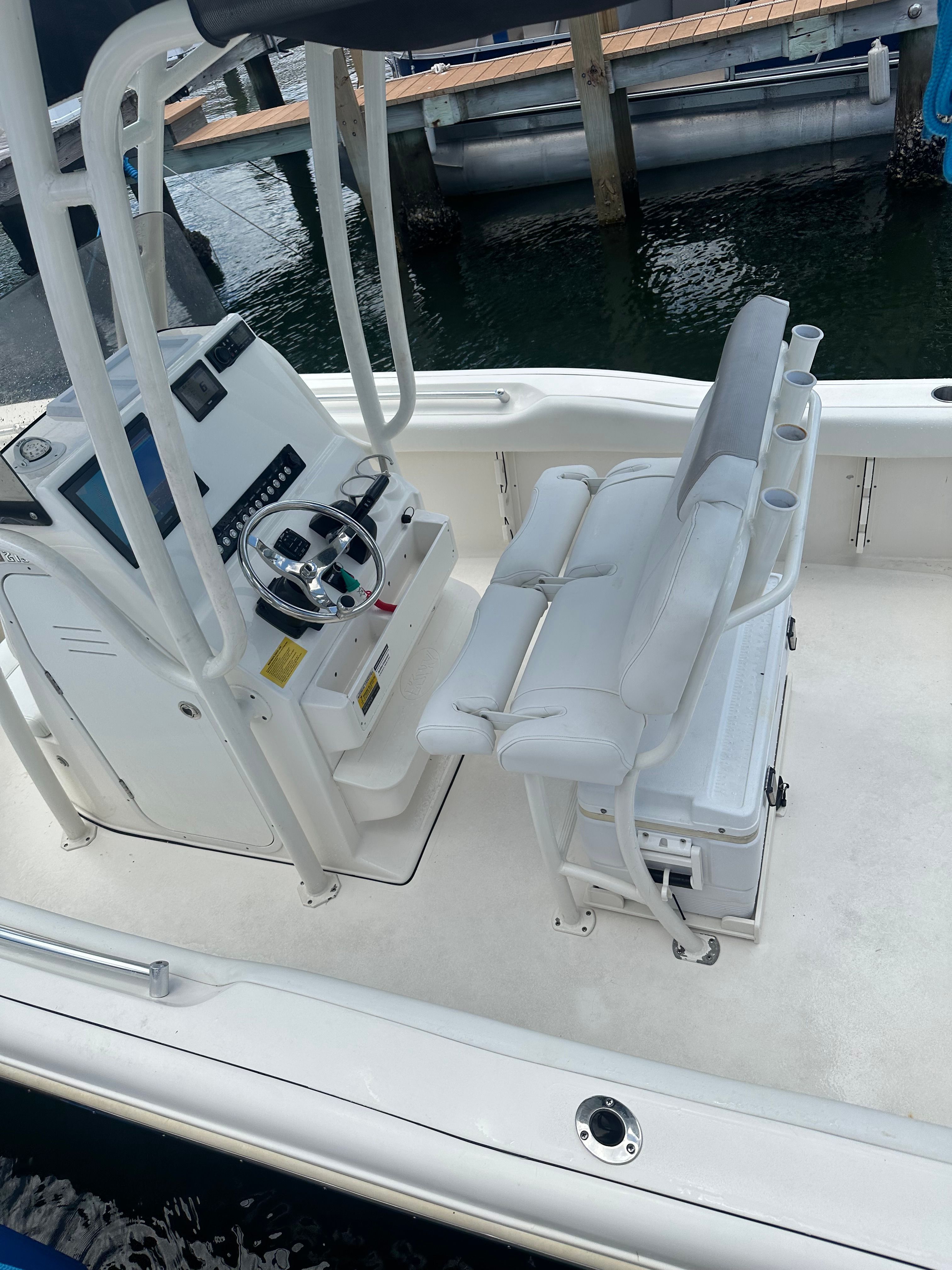 A modern boat with white interior and helm station, docked at a pier.