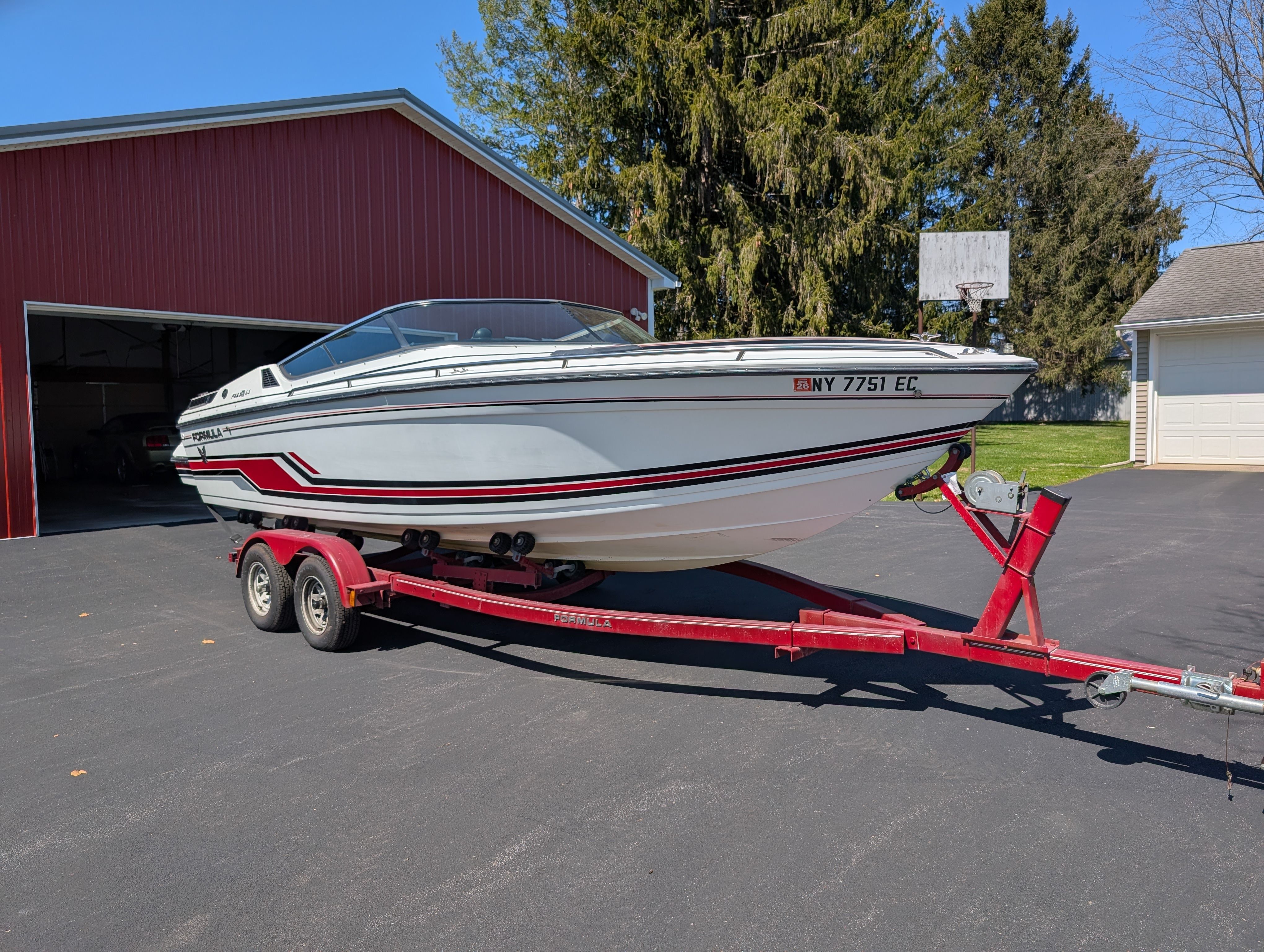 A white 1989 Formula F223LS boat on a red trailer, parked in front of a garage.