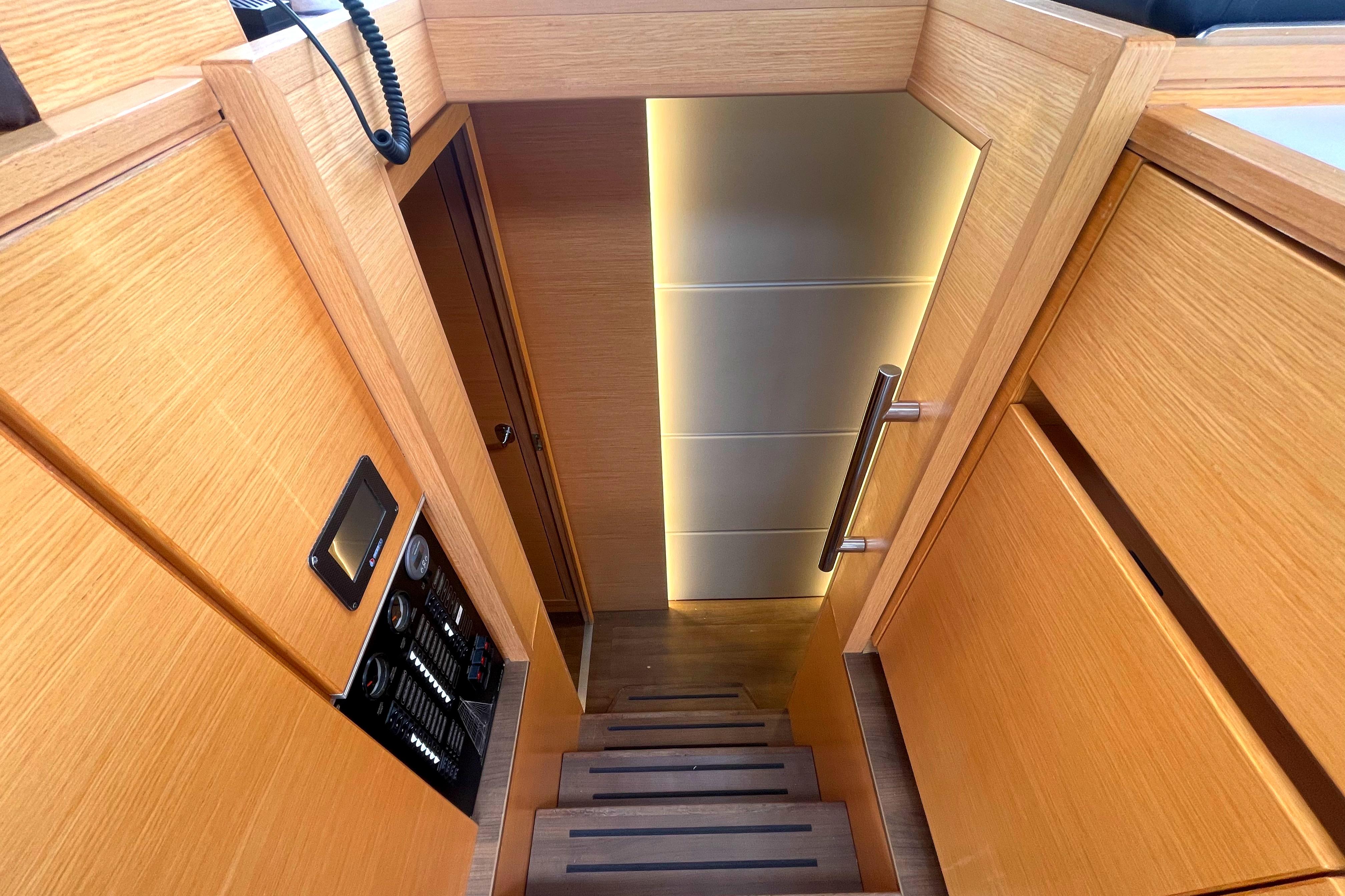 Stairway inside 2019 Bavaria Nautitech 46 FLY yacht with wooden finish and control panel.