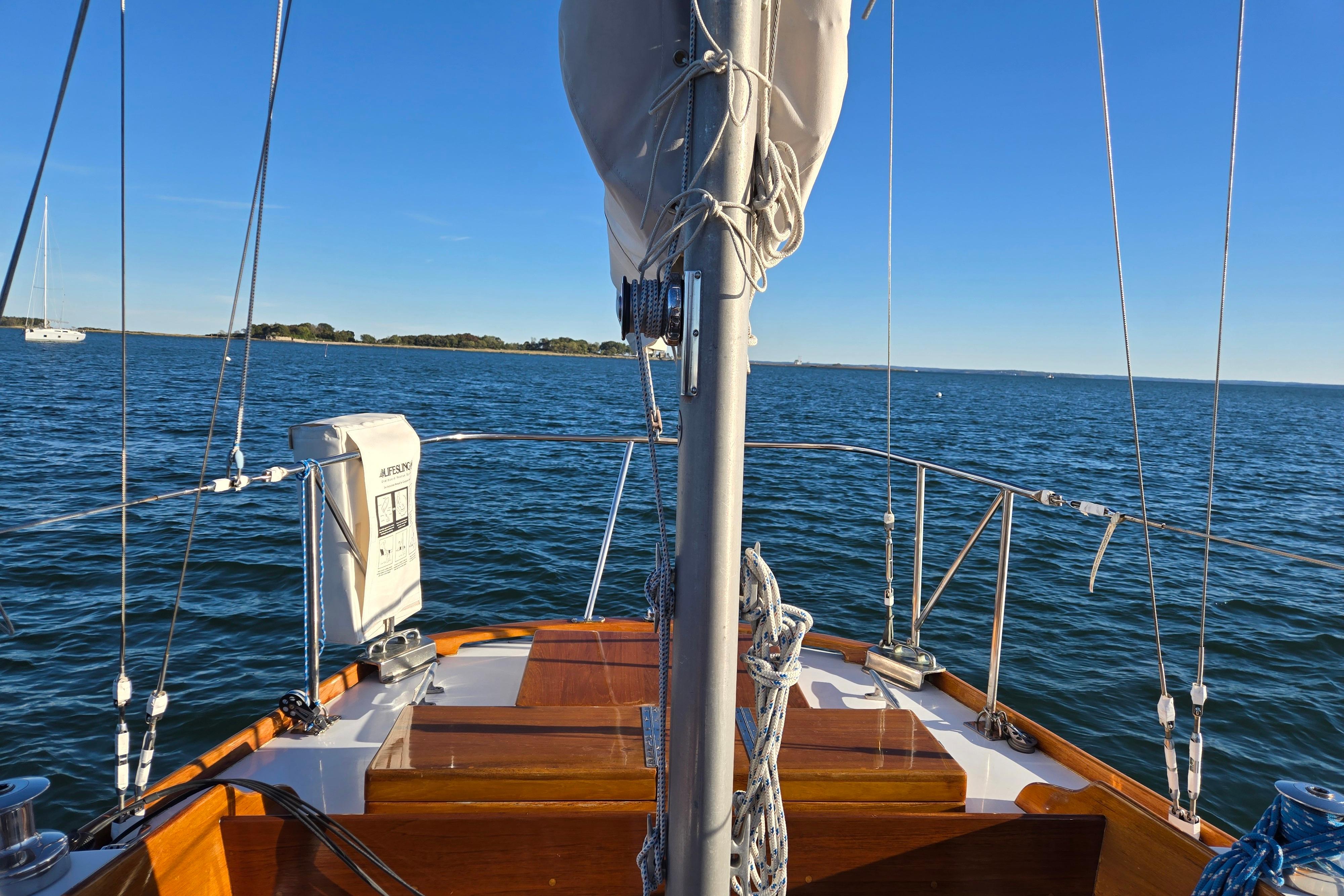 1970 Hinckley Bermuda 40 sailboat on open water, clear blue sky, and distant shoreline.