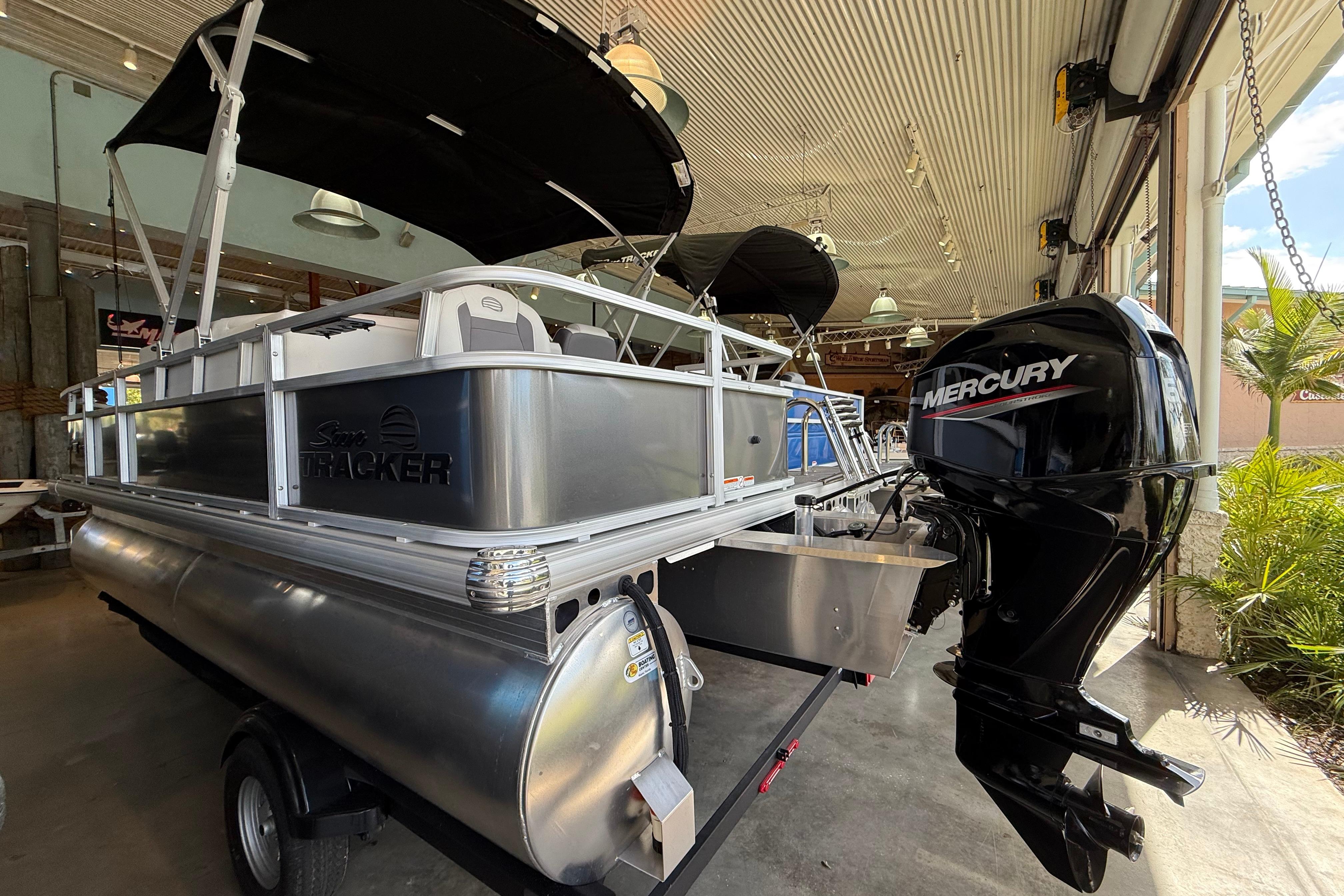 2026 Sun Tracker Bass Buggy 18 DLX pontoon boat with Mercury outboard motor in showroom.