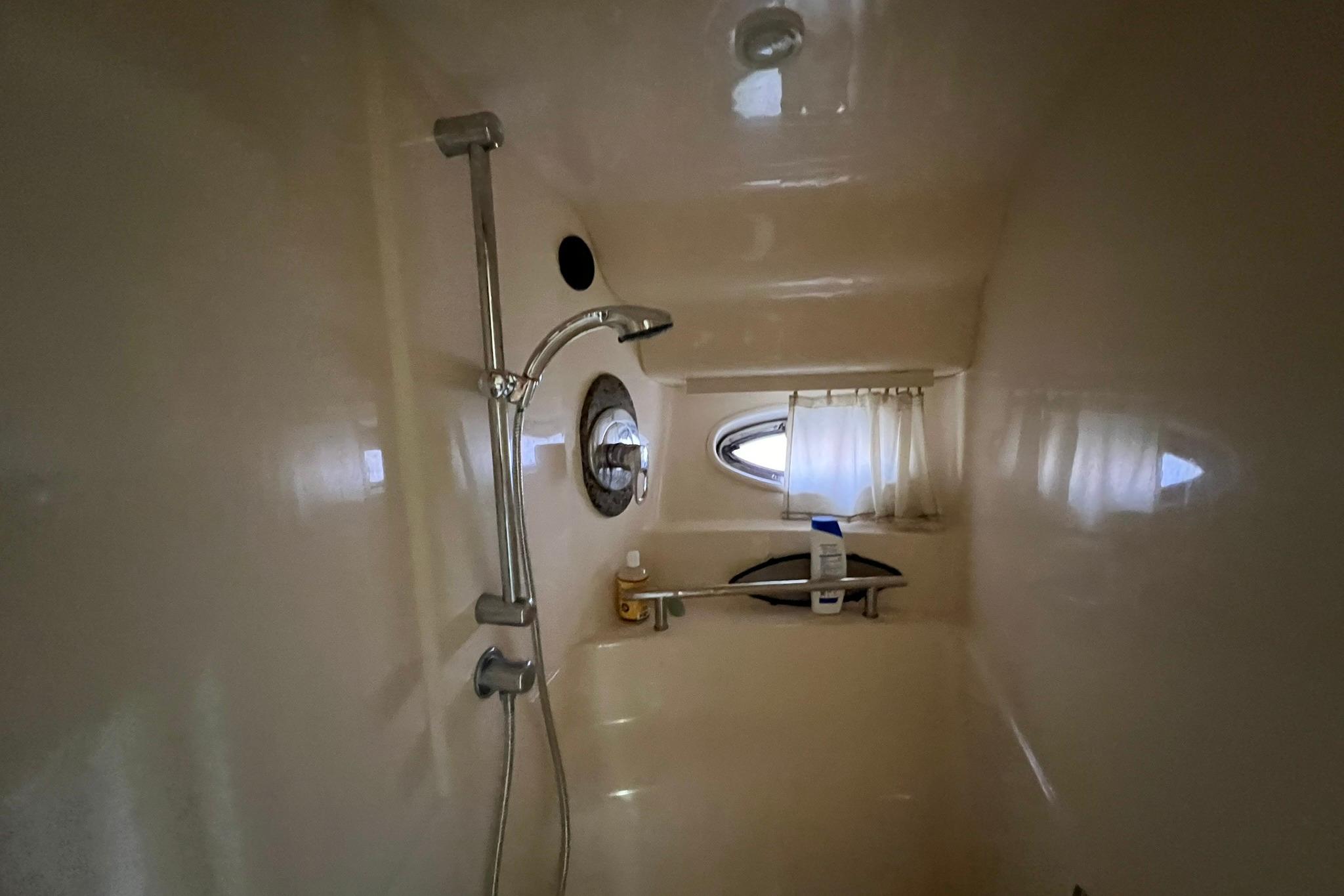Shower area inside 2005 Sea Ray 390 Sundancer yacht, featuring a porthole and showerhead.