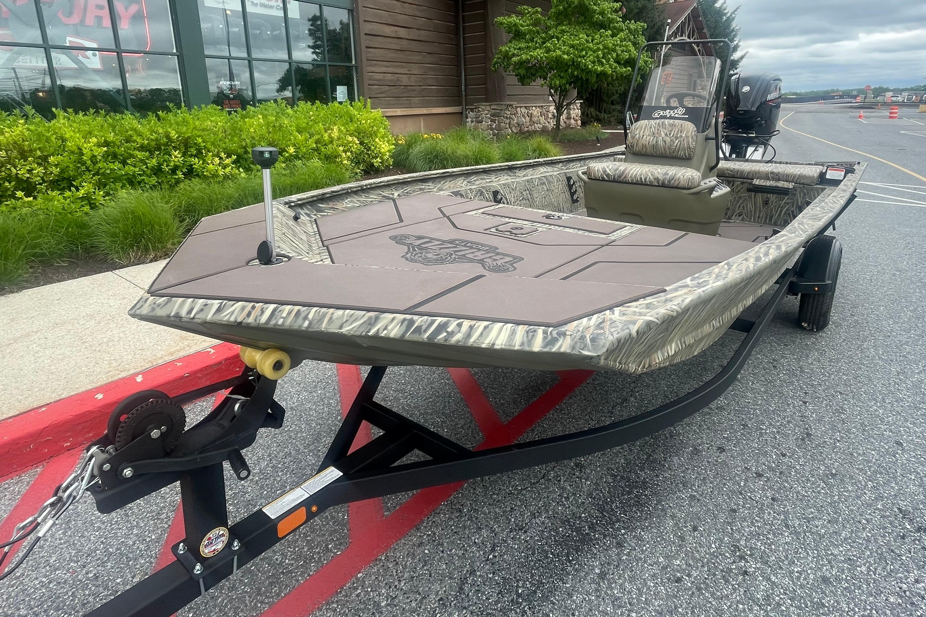 2026 Tracker Grizzly 1860 CC boat on trailer, parked outdoors near greenery.