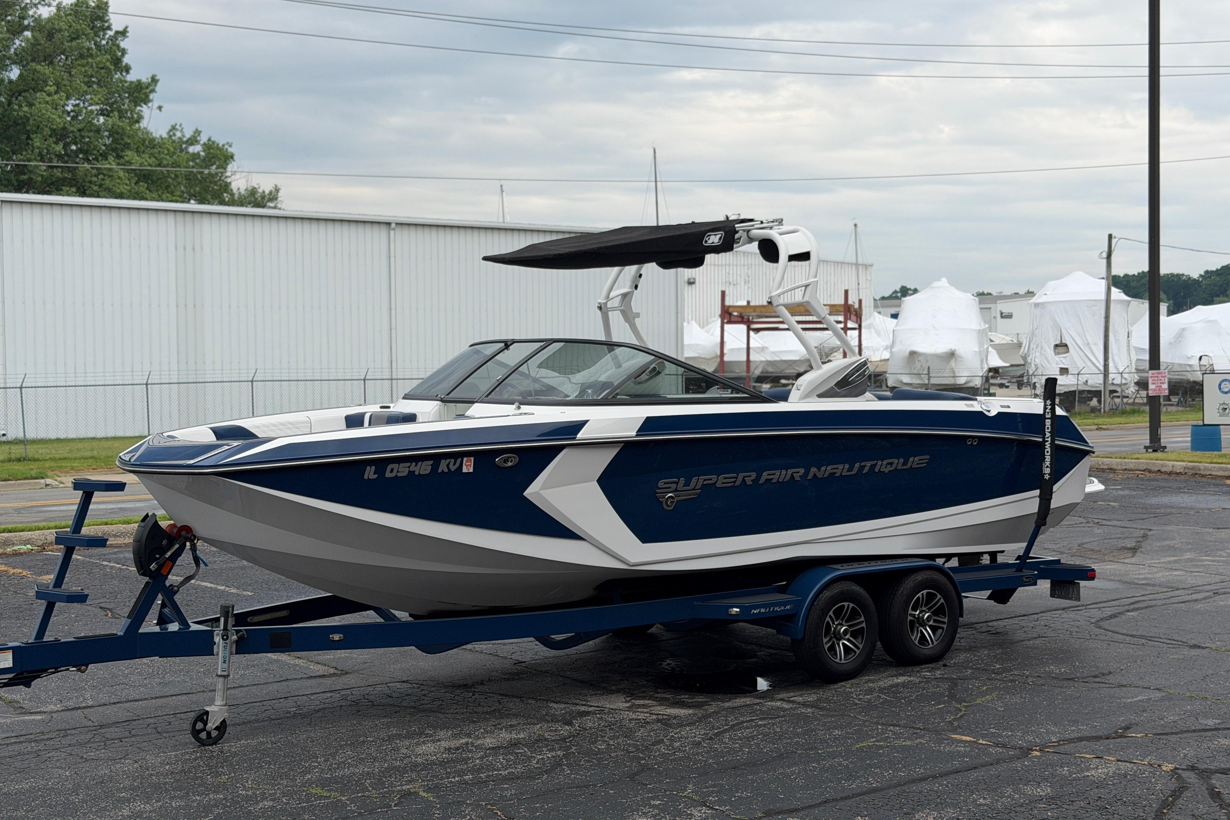 2016 Naitique G25 boat on trailer, blue and white design, parked outdoors.