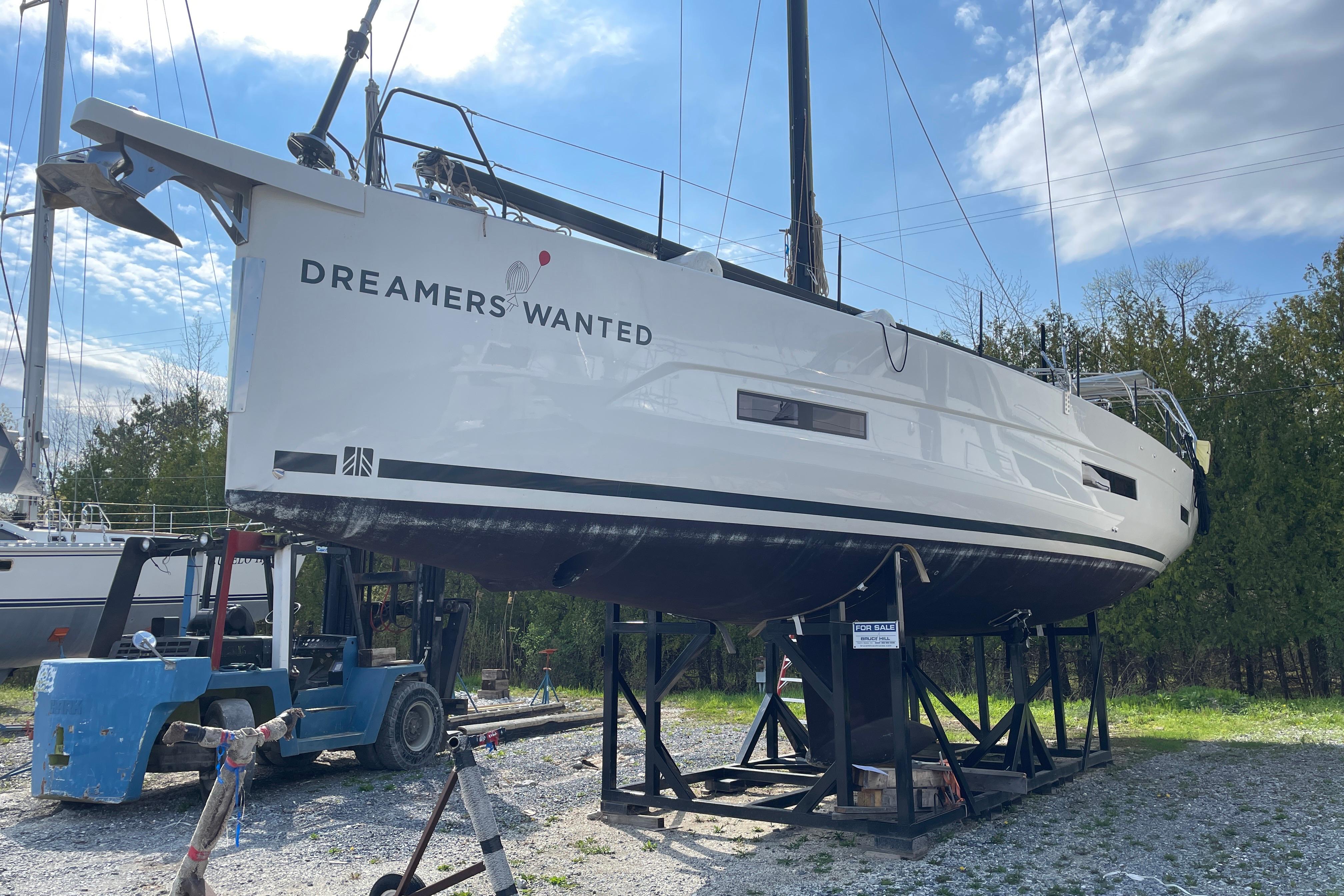 2022 Dufour 530 sailboat on stands, "Dreamers Wanted" text, under a partly cloudy sky.