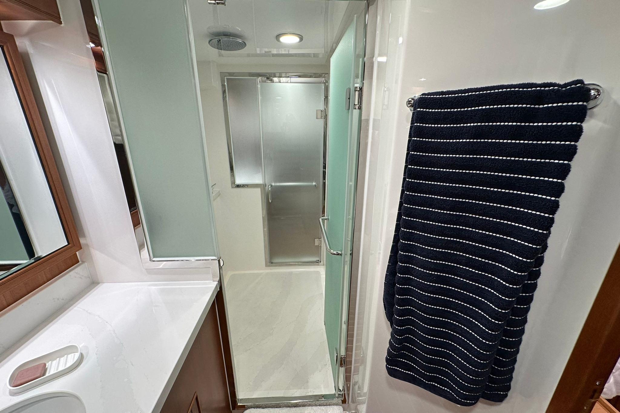 Modern bathroom in 2023 Marlow Explorer 66E-CB yacht with sleek shower and striped towel.