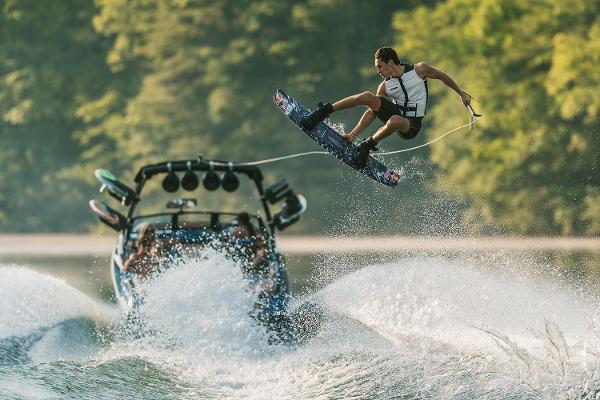 Manufacturer Provided Image: Wakeboarder performing a trick behind a 2021 Axis A24 boat on a lake.
