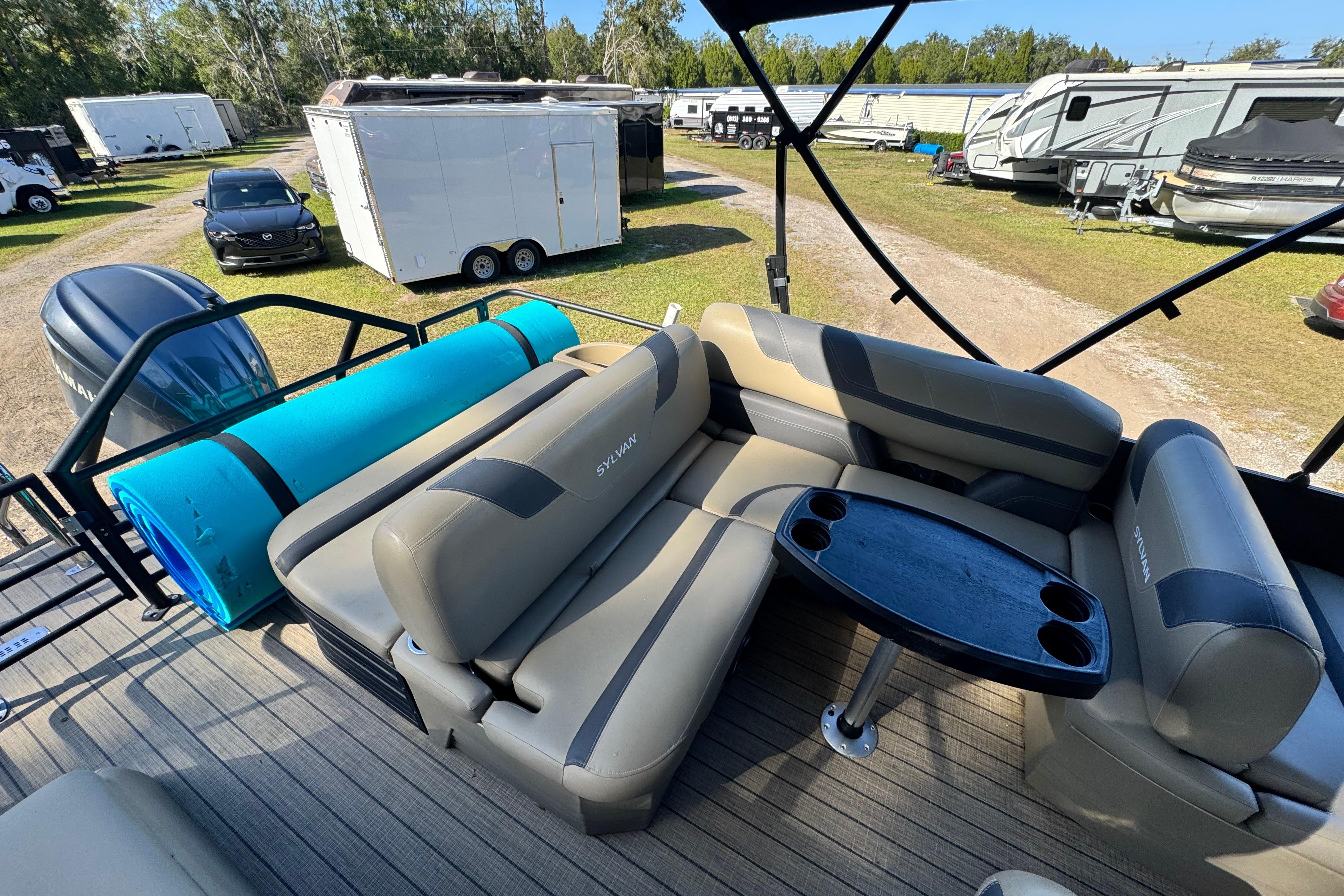 2023 Sylvan L5 CLZ pontoon boat interior with seating and table, parked near trailers.