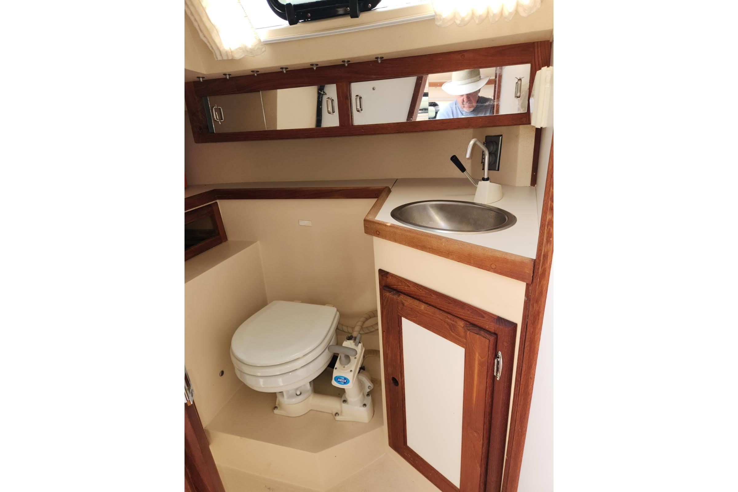1990 Catalina Capri boat bathroom with toilet, sink, and mirrored cabinet.