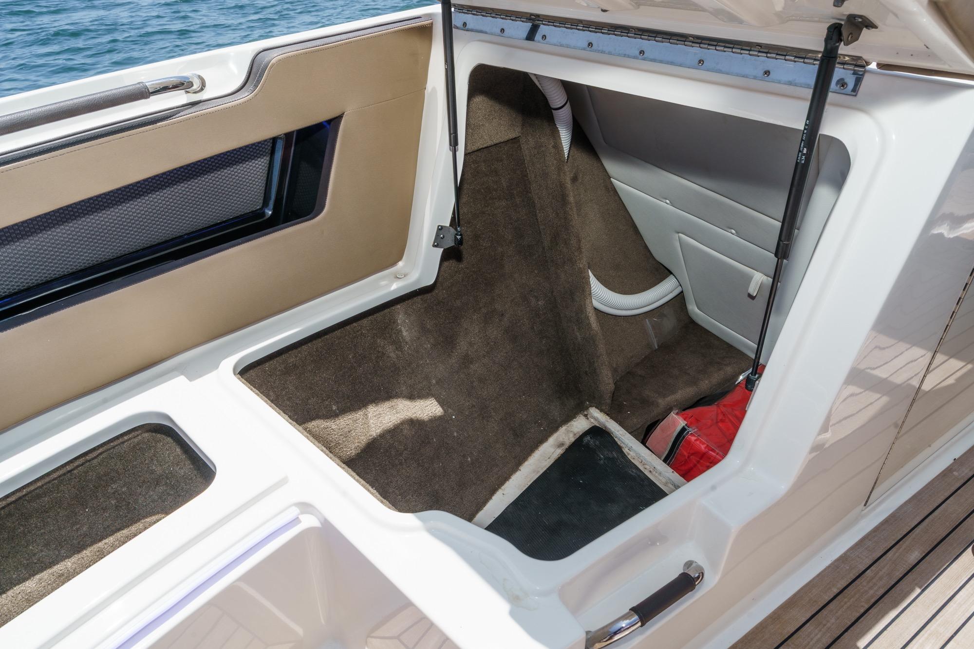 An open storage compartment on a boat with brown carpeting and a red item inside.