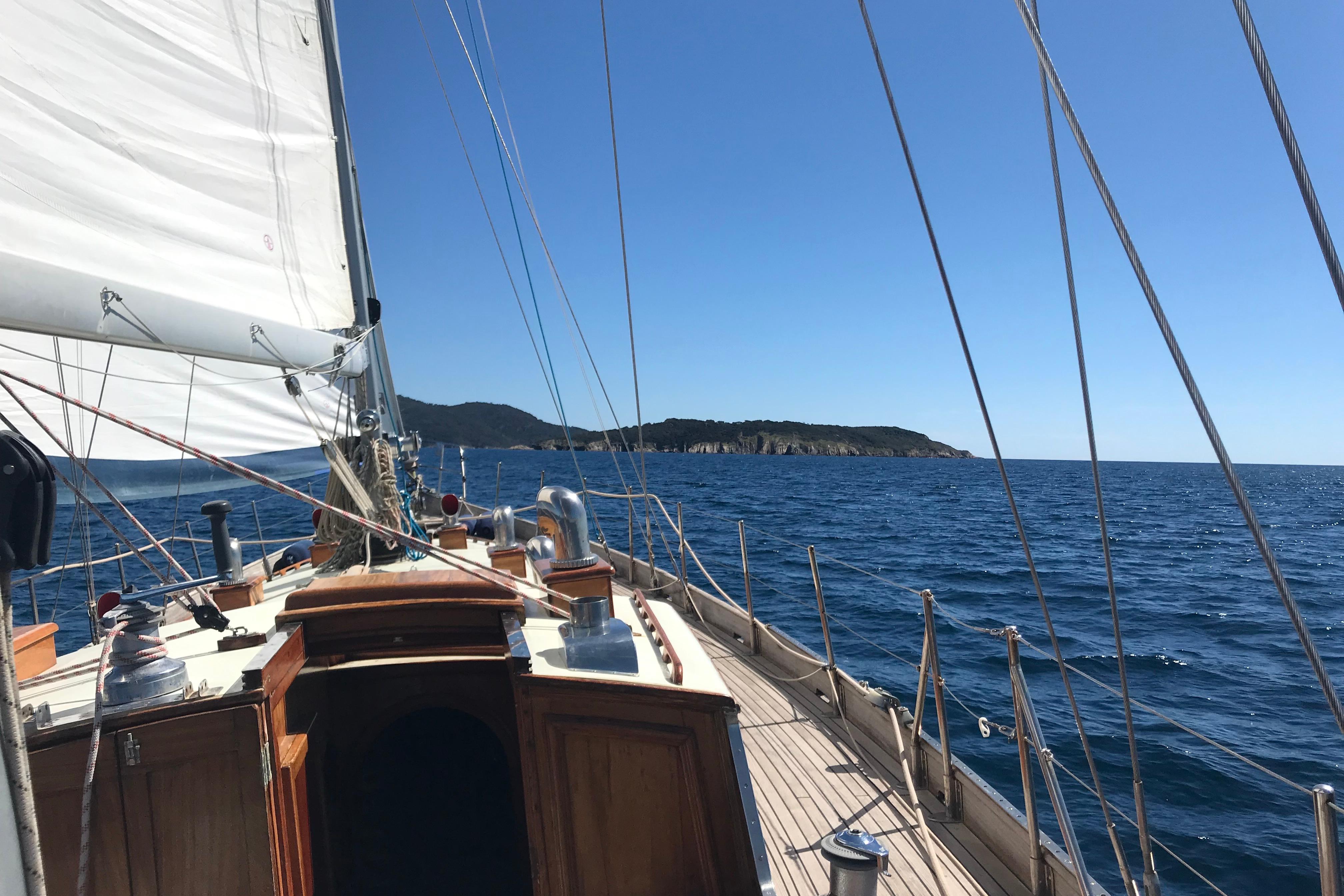 Sailing on a 1958 Costantini Ketch Marconi, with clear blue sea and distant coastline.