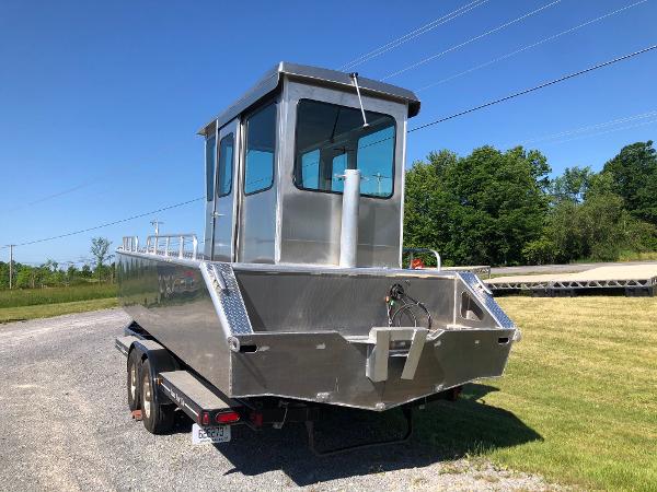 A modern workboat with an aluminum hull sits on a trailer in a grassy area.