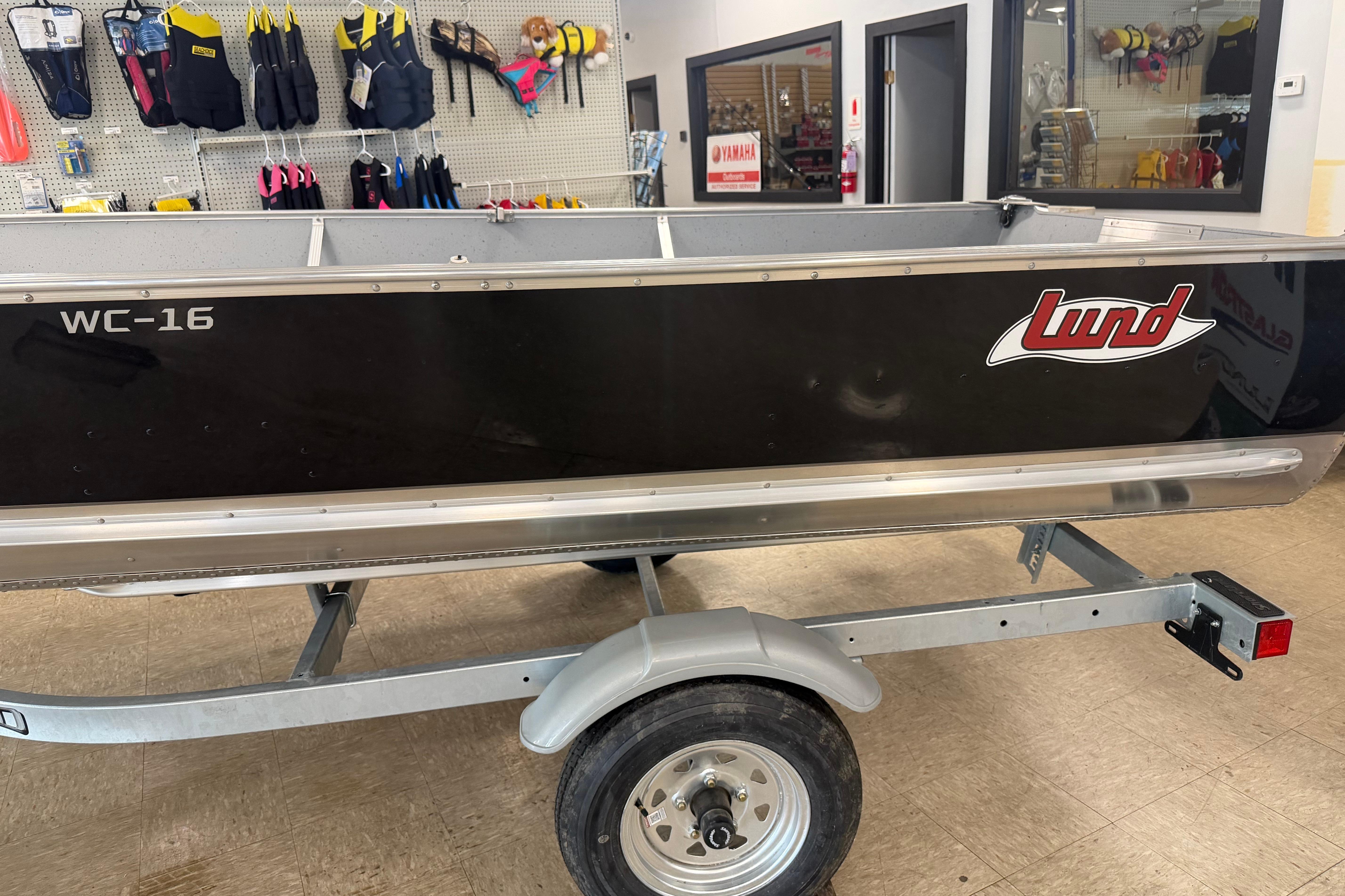 2027 Lund WC 16 boat on trailer in showroom with life jackets displayed.