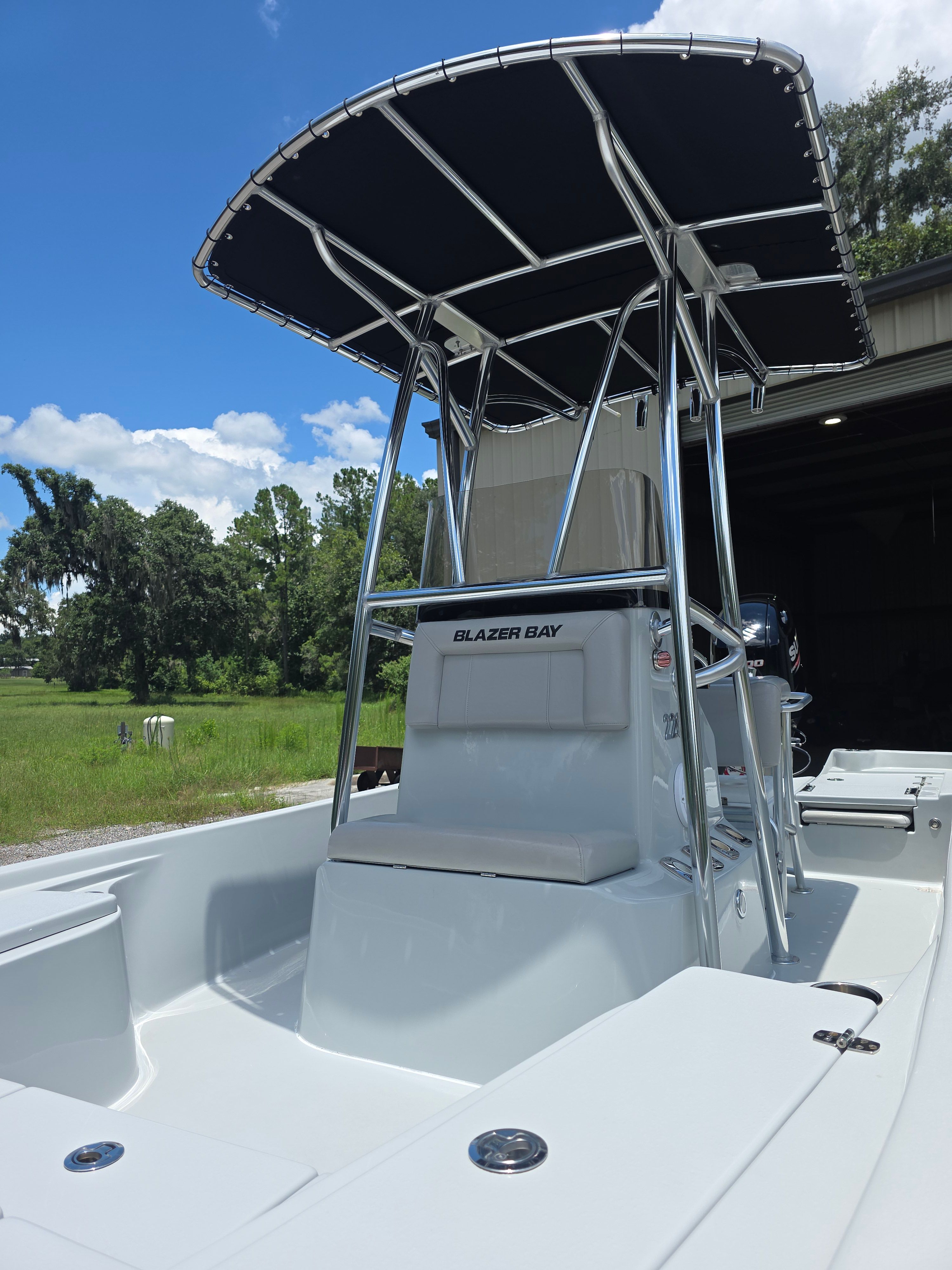 A 2019 Blazer Bay 2200 with a T-top, parked outdoors, surrounded by trees and grass.