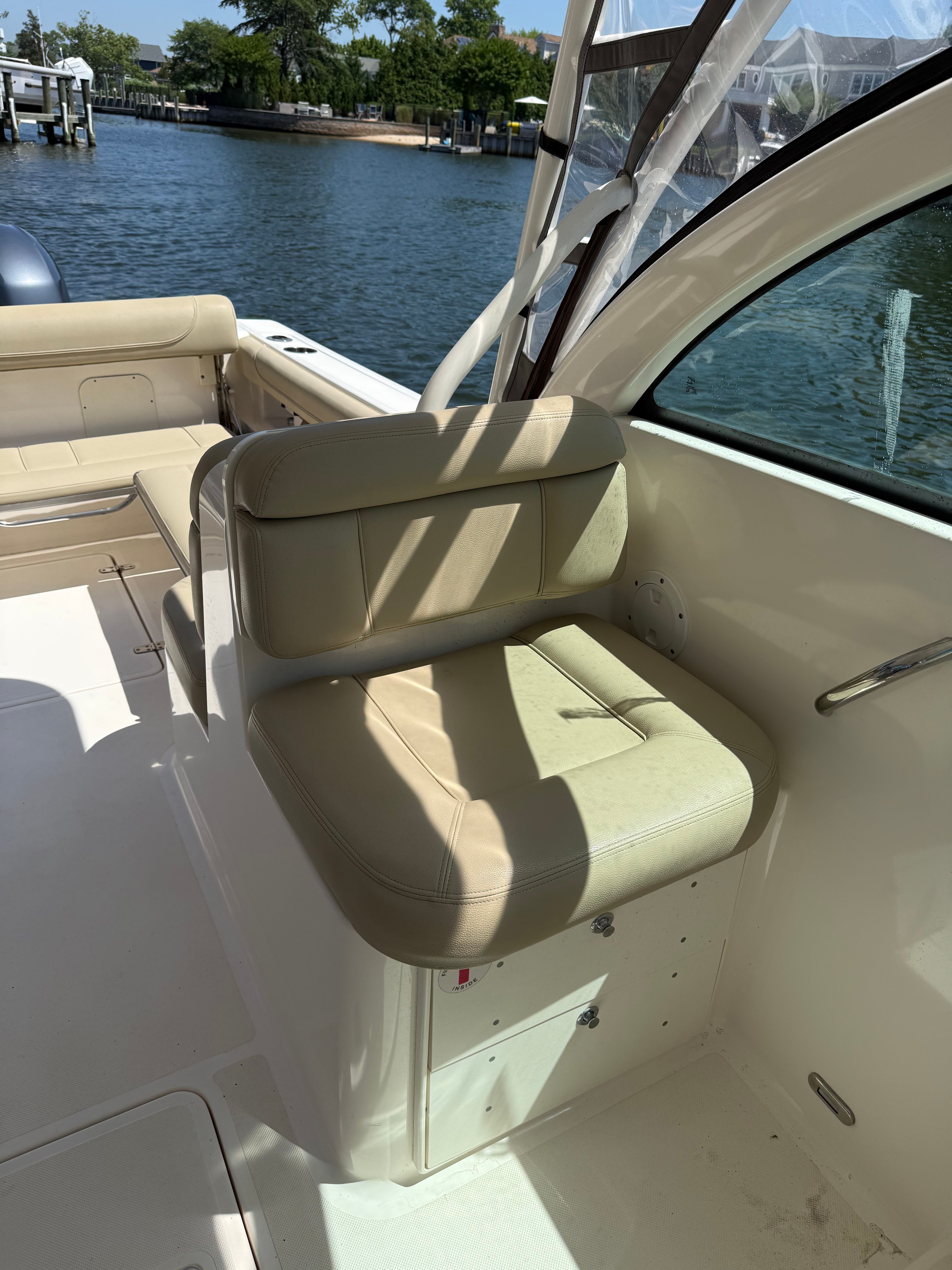 A seat on a boat overlooking the water with a dock in the background.