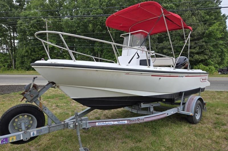 1996 Boston Whaler Outrage 17 boat with red canopy on trailer, parked on grass.