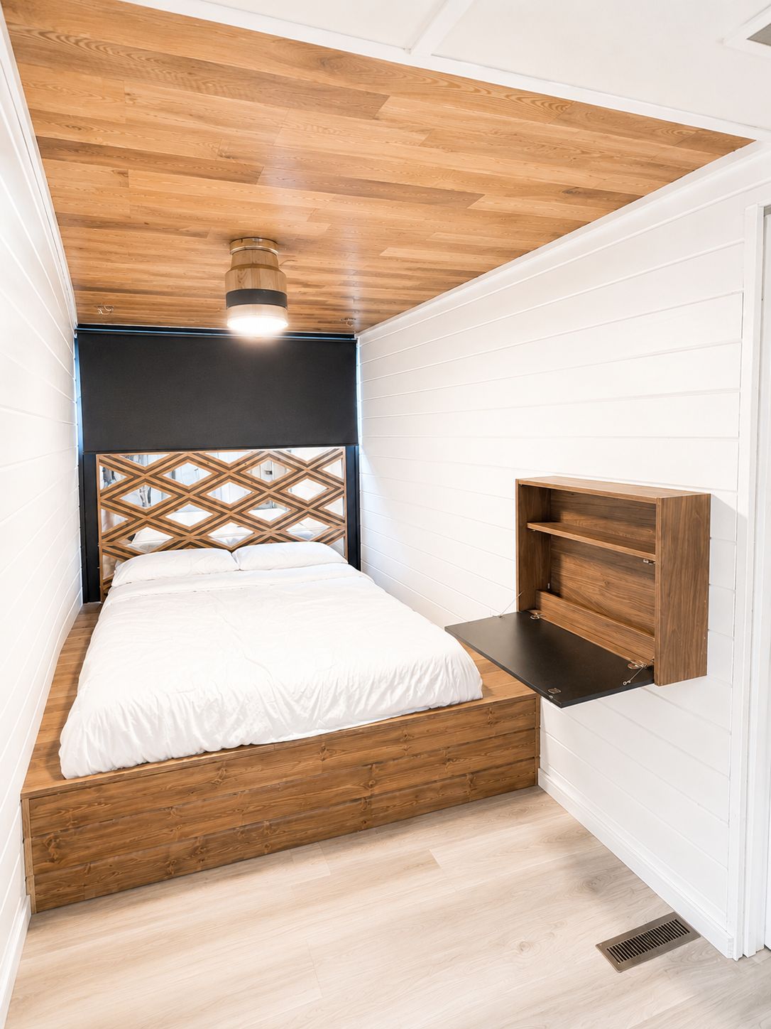 A cozy bedroom with wooden floor and ceiling, a double bed, and a foldable table.
