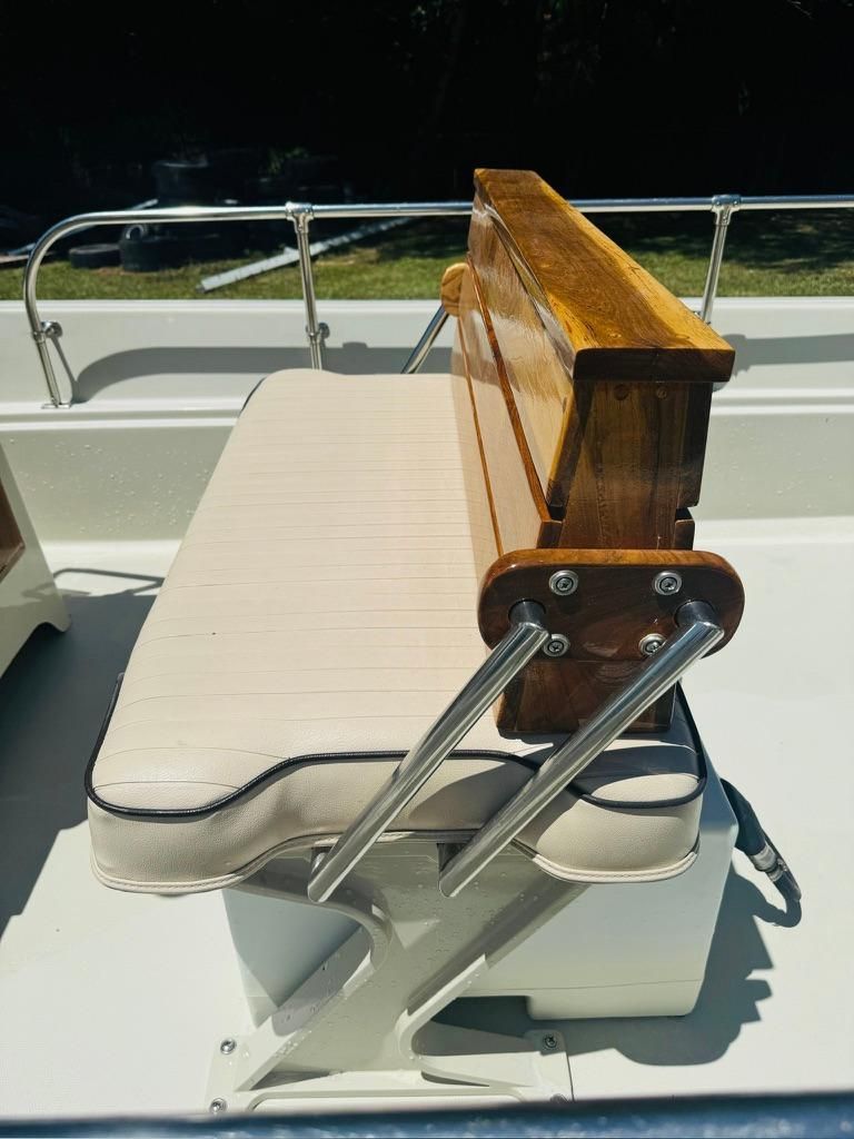 A white bench seat with a wooden backrest and metal supports on a boat.