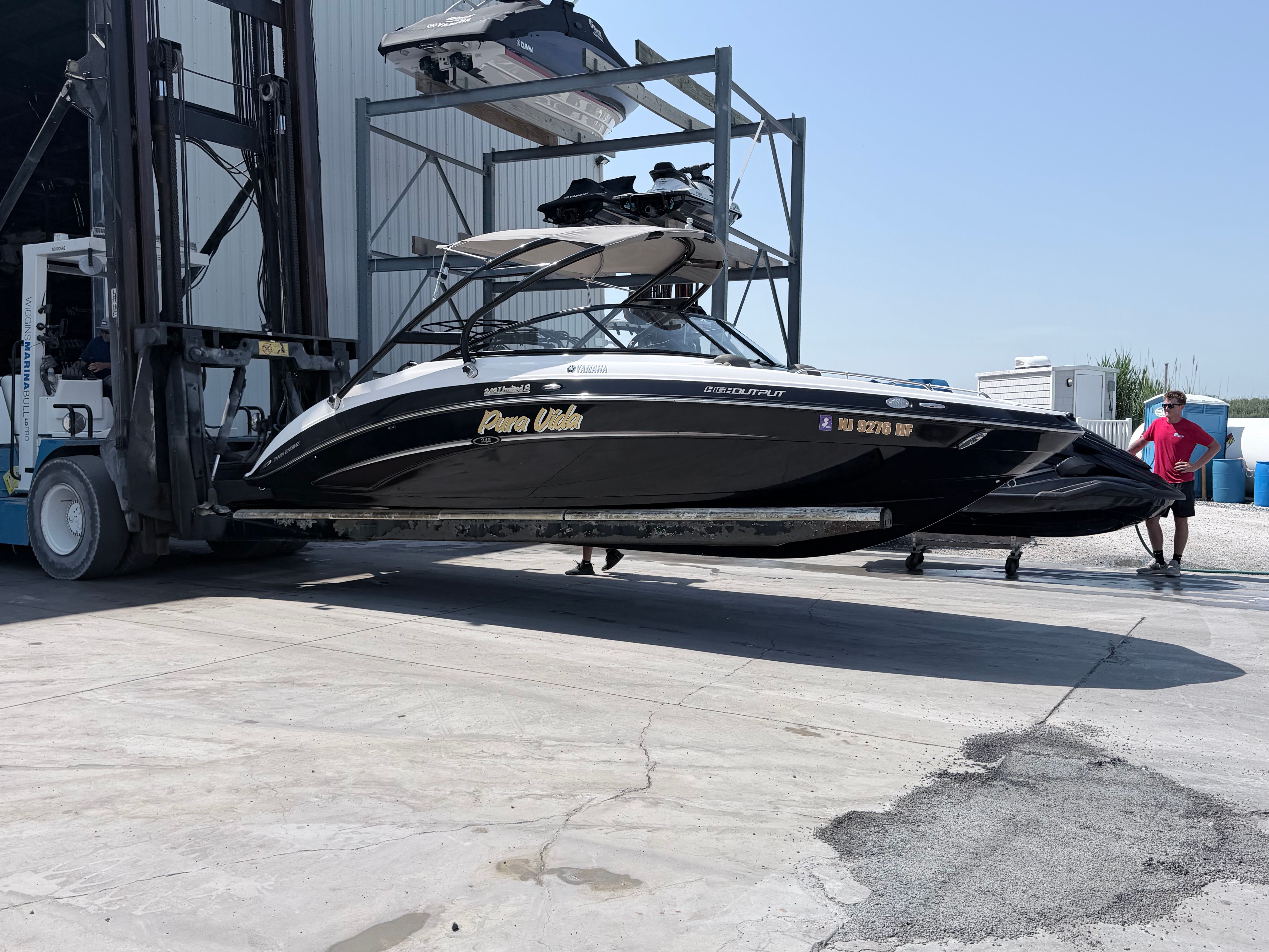 A black Yamaha boat is being carried by a forklift on a concrete lot.