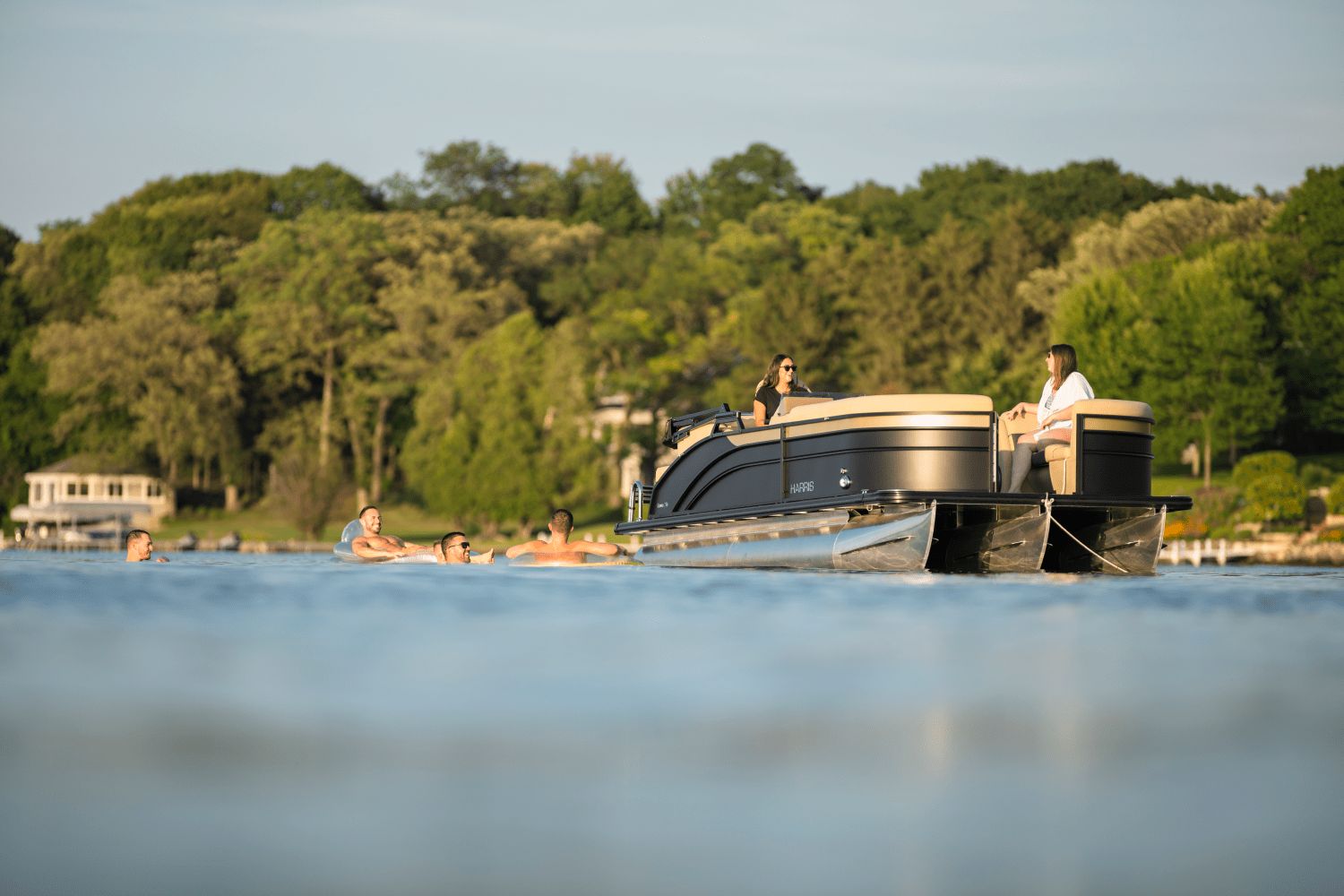 A 2026 Harris Cruiser 230 on a calm lake, surrounded by swimmers.