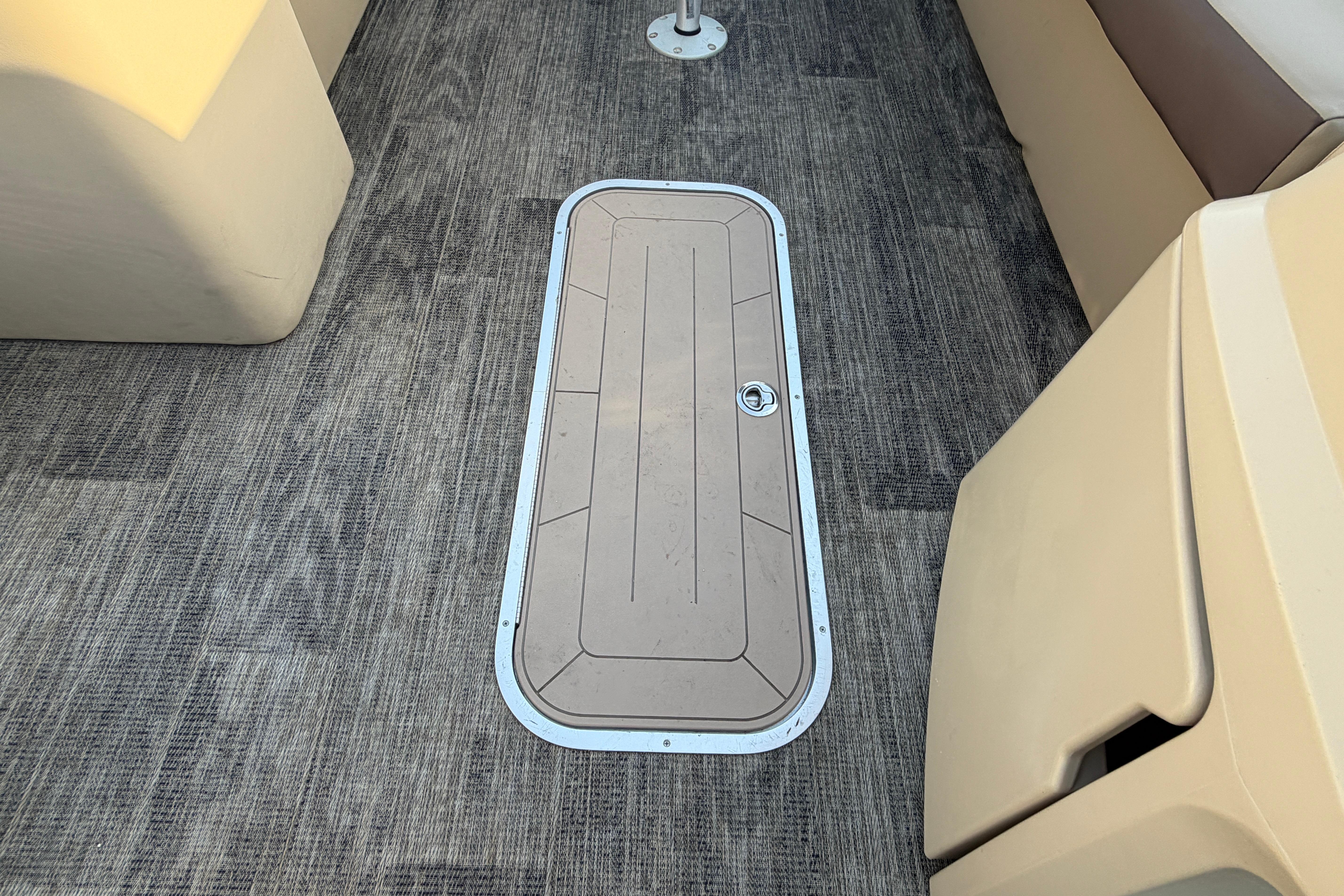 Floor hatch on 2023 Godfrey Sweetwater 2286 C boat, featuring textured carpet and beige seating.