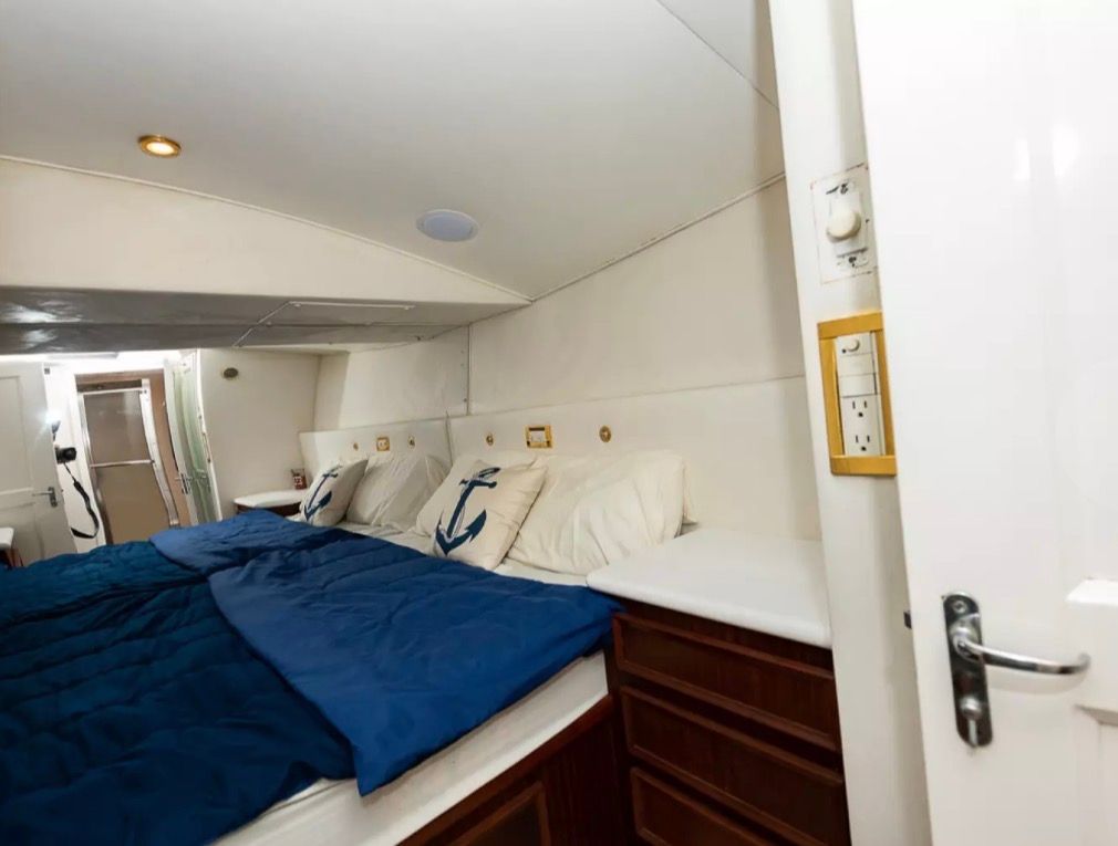 Interior of a 1979 Hatteras Sport fishing yacht with a cozy bed and nautical-themed pillows.