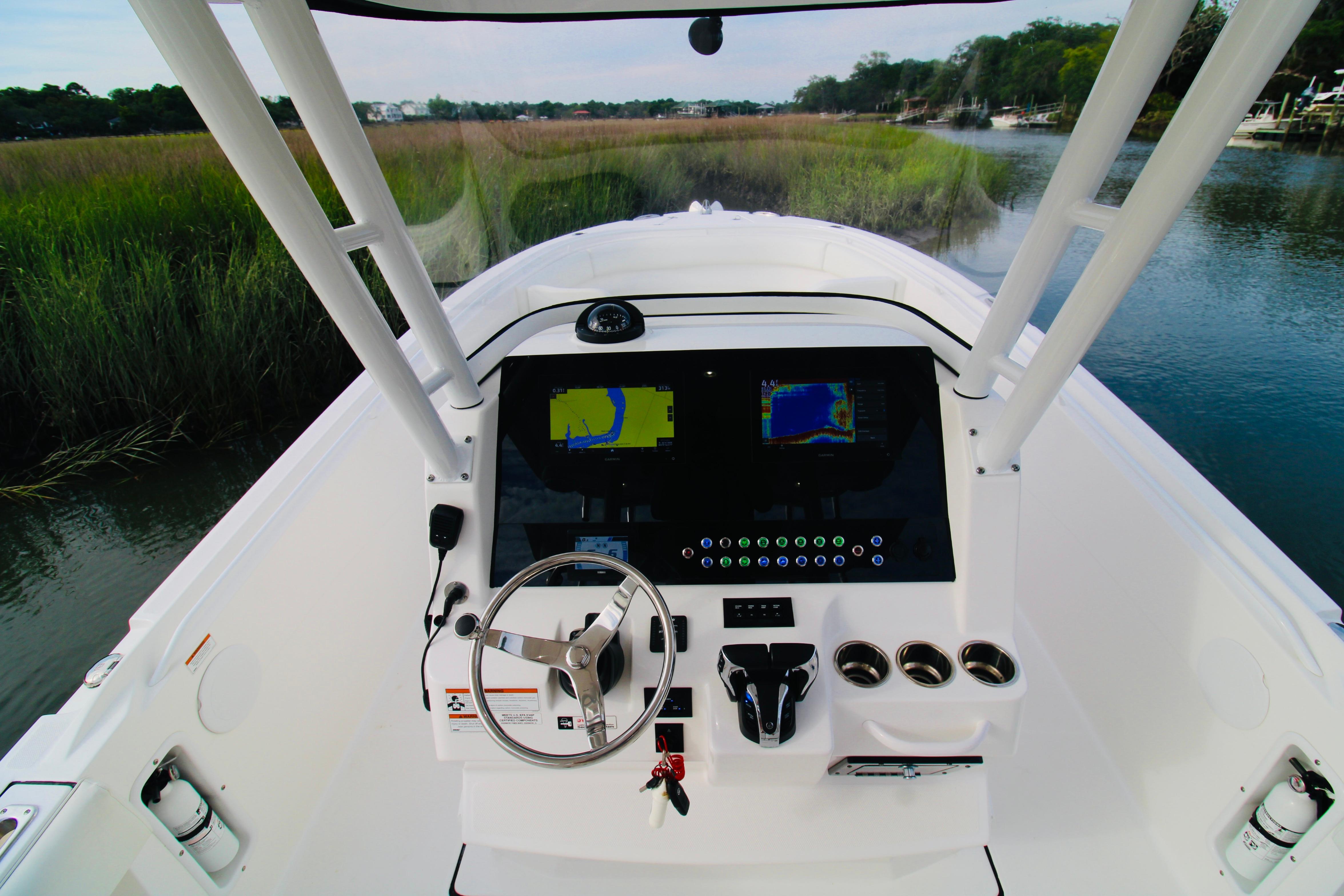 2022 Edgewater 280CC boat dashboard with navigation screens and steering wheel, surrounded by scenic waterway.