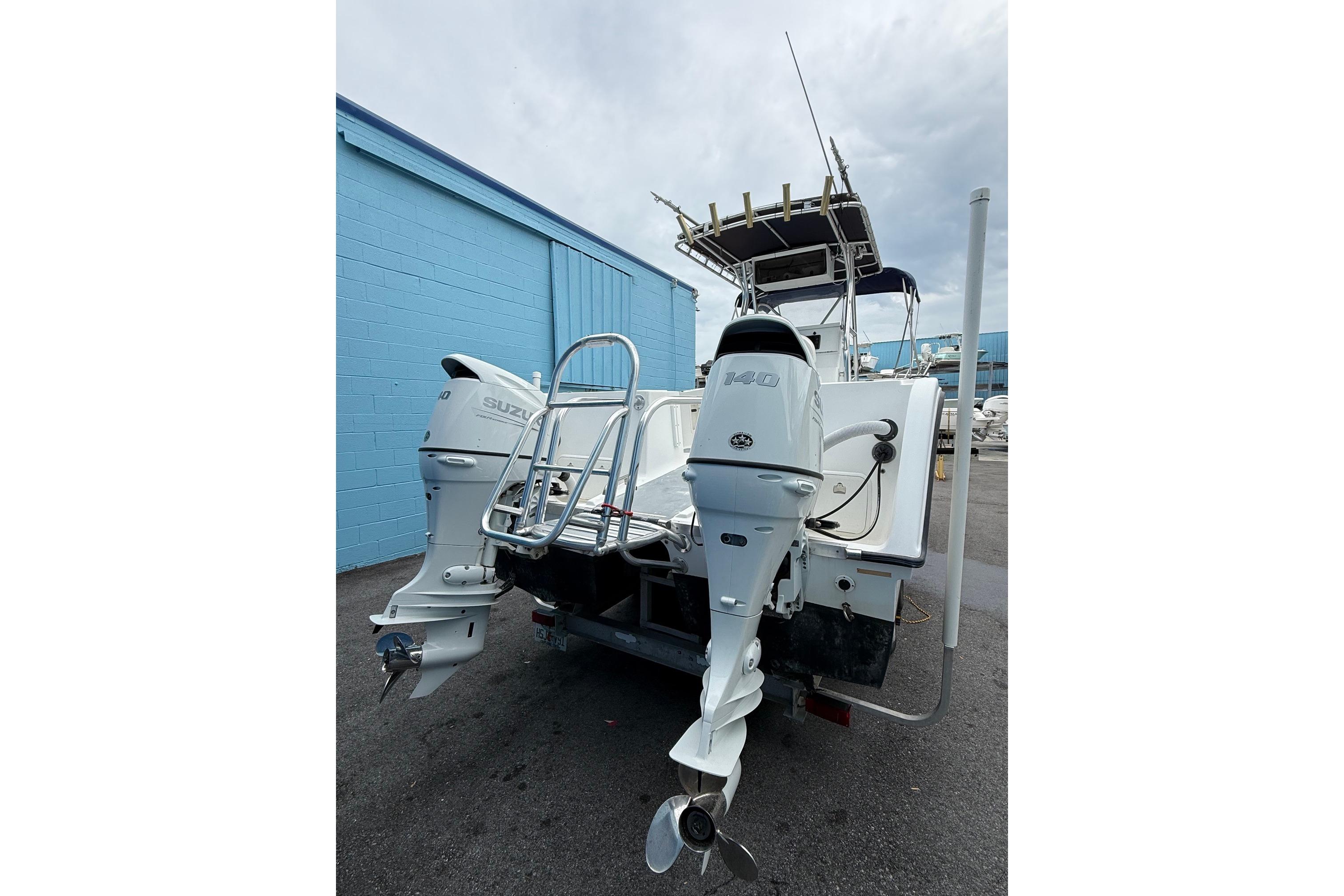 2002 Pro Sports 2200 CC ProKat boat with dual Suzuki outboard motors, parked near a blue building.