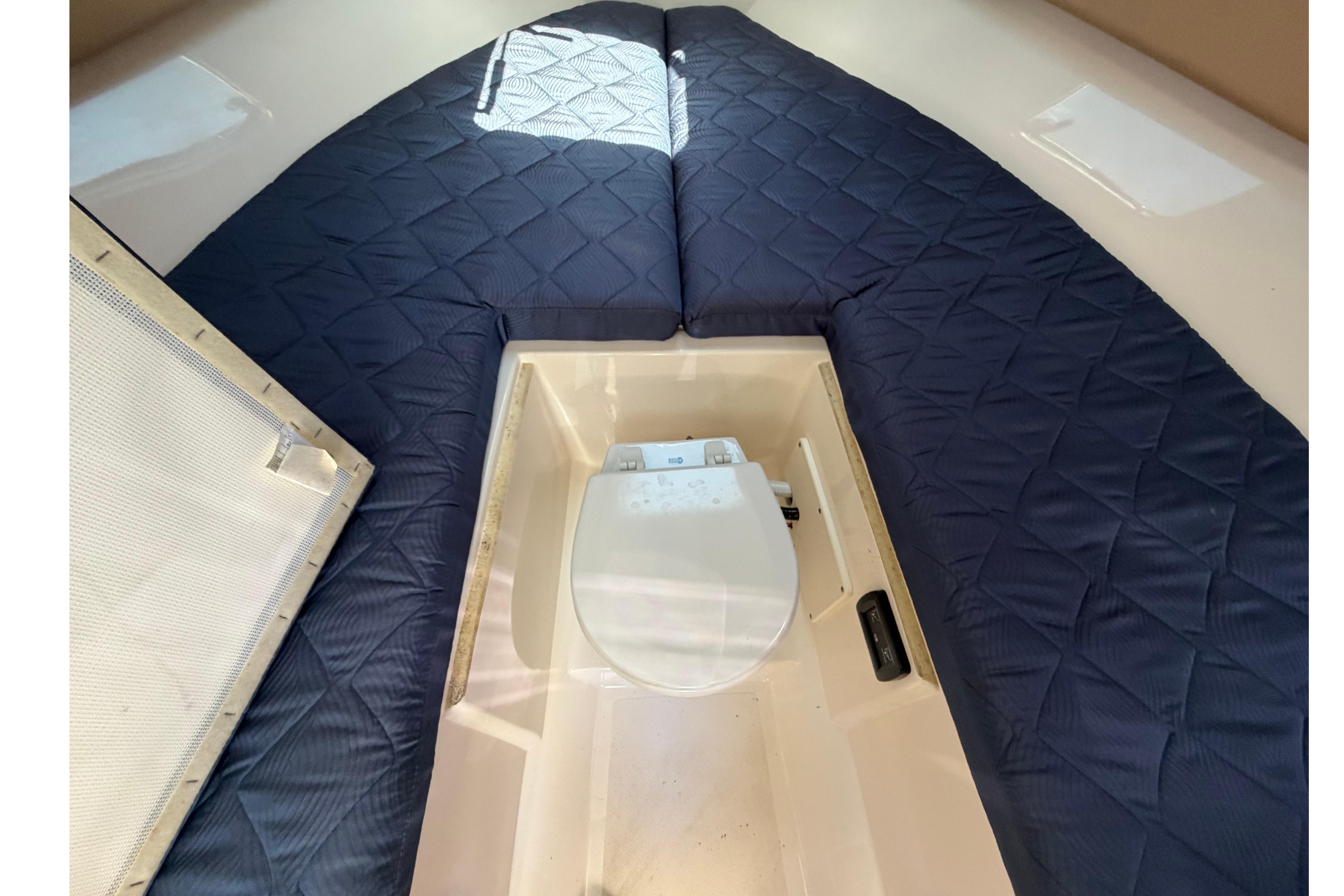 2010 Pursuit OS 255 Offshore cabin interior with blue cushions and a compact toilet.