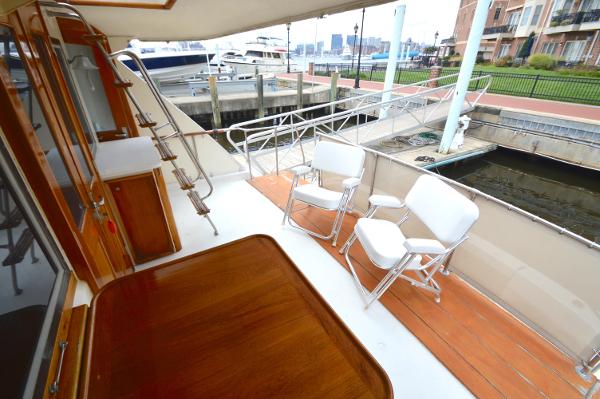 The image shows the deck of a 1980 Hatteras 53 Yacht Fisherman, with white chairs and a wooden table.