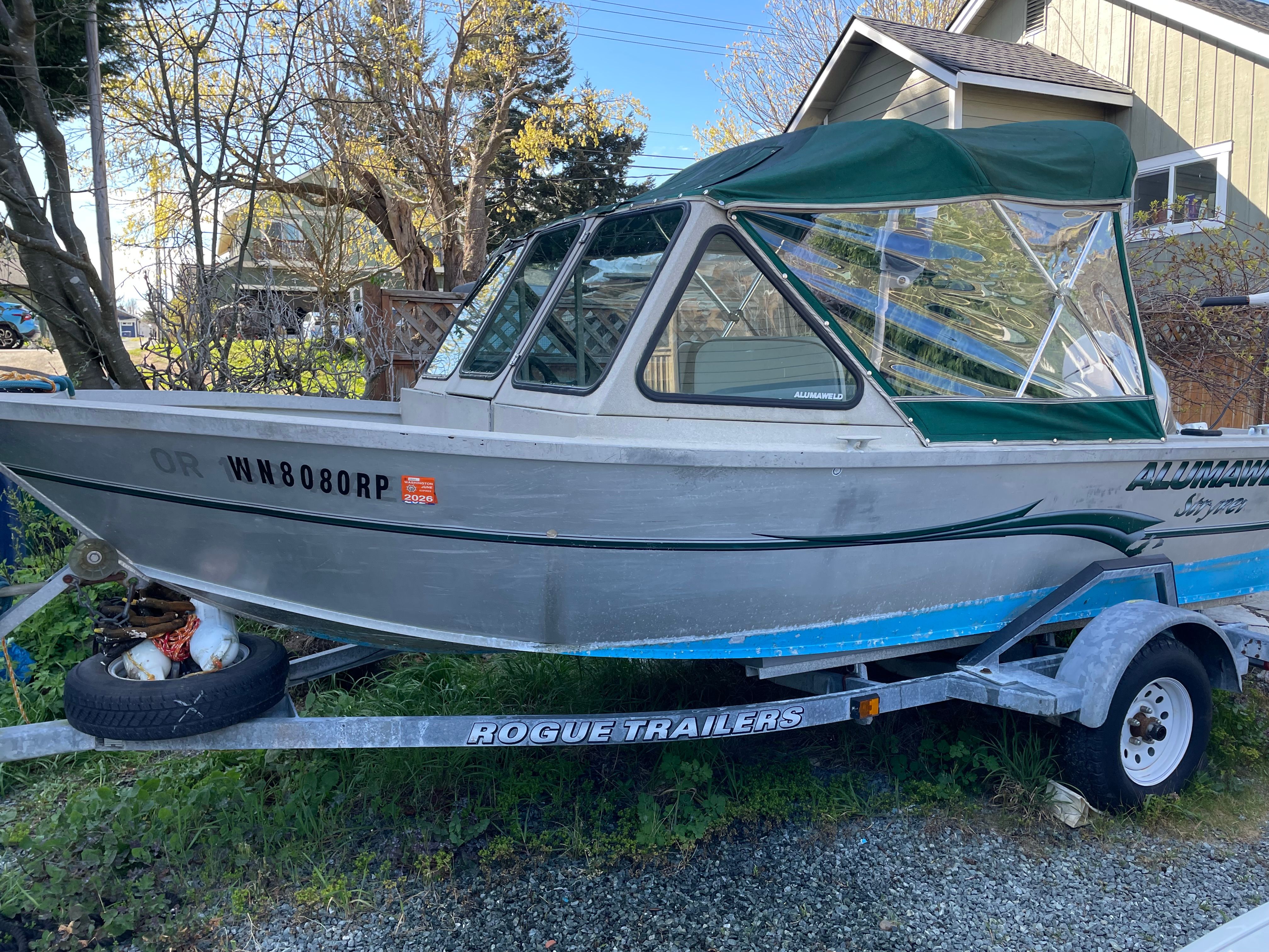 A 2001 Alumaweld Stryker boat on a trailer, with a green canopy, parked outdoors.