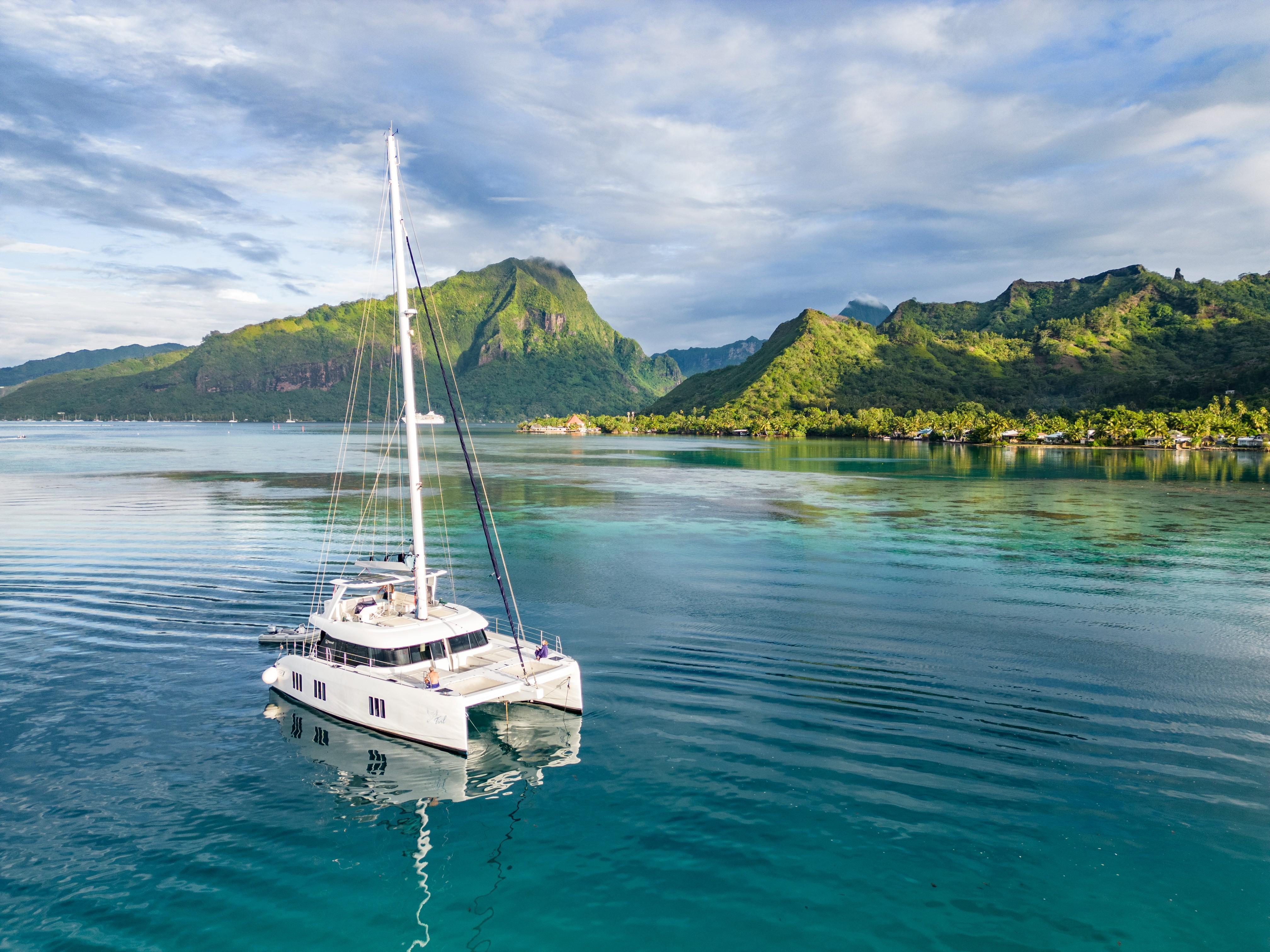 Sunreef 50 catamaran sailing in tranquil waters with lush mountains in the background, 2019 model.