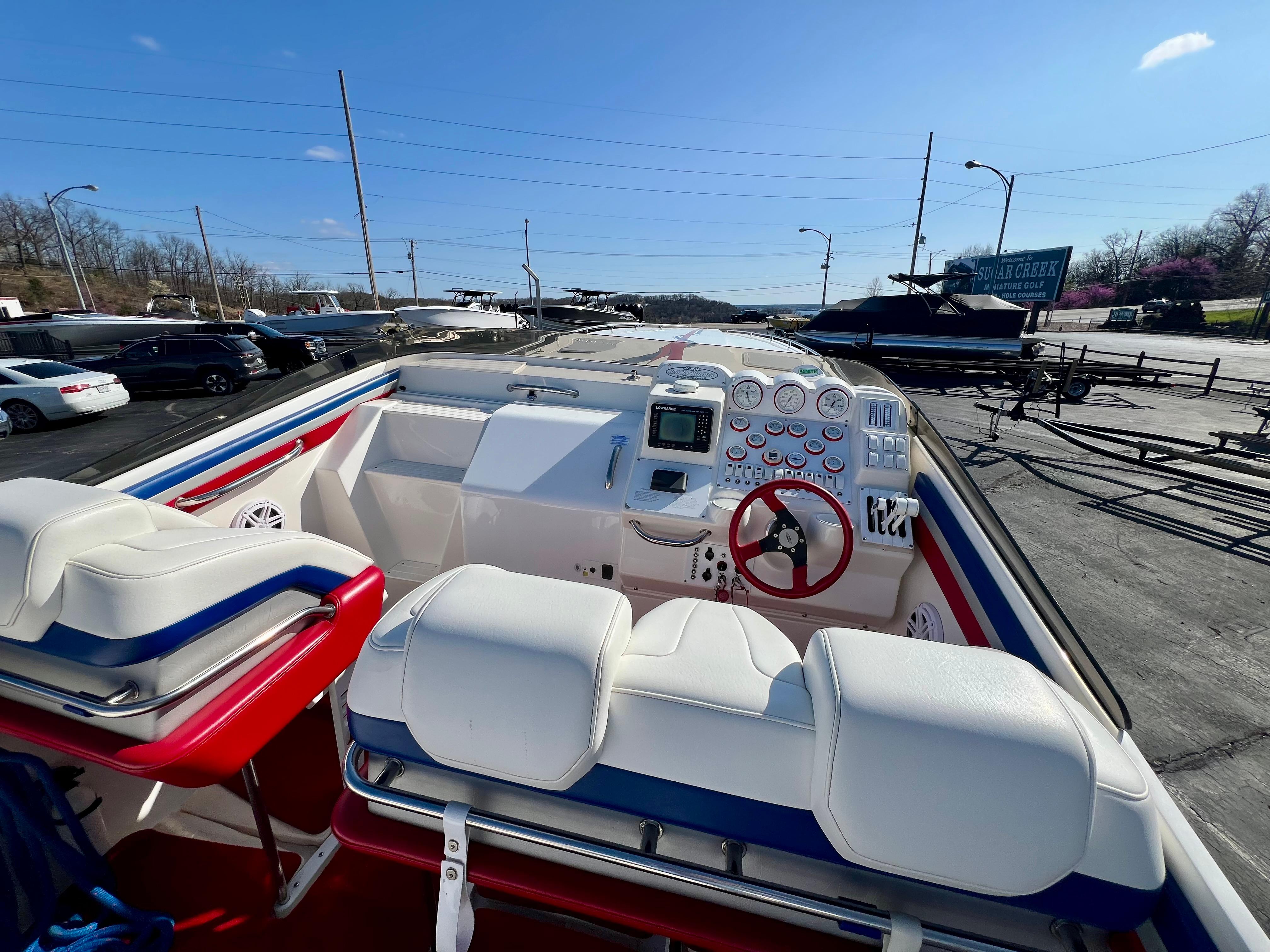 1999 Black Thunder 430 Flat Deck boat with white seating and red accents, docked outdoors.