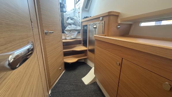 Interior of 2025 Nimbus T11 boat with wooden cabinetry and compact stairs.
