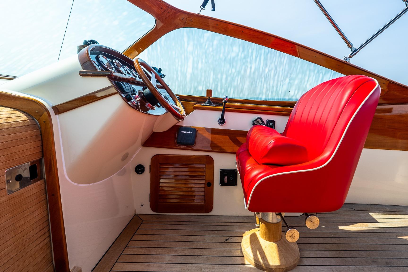 Red captain's chair and helm of 2005 Hinckley Talaria 29R boat, featuring wooden accents.