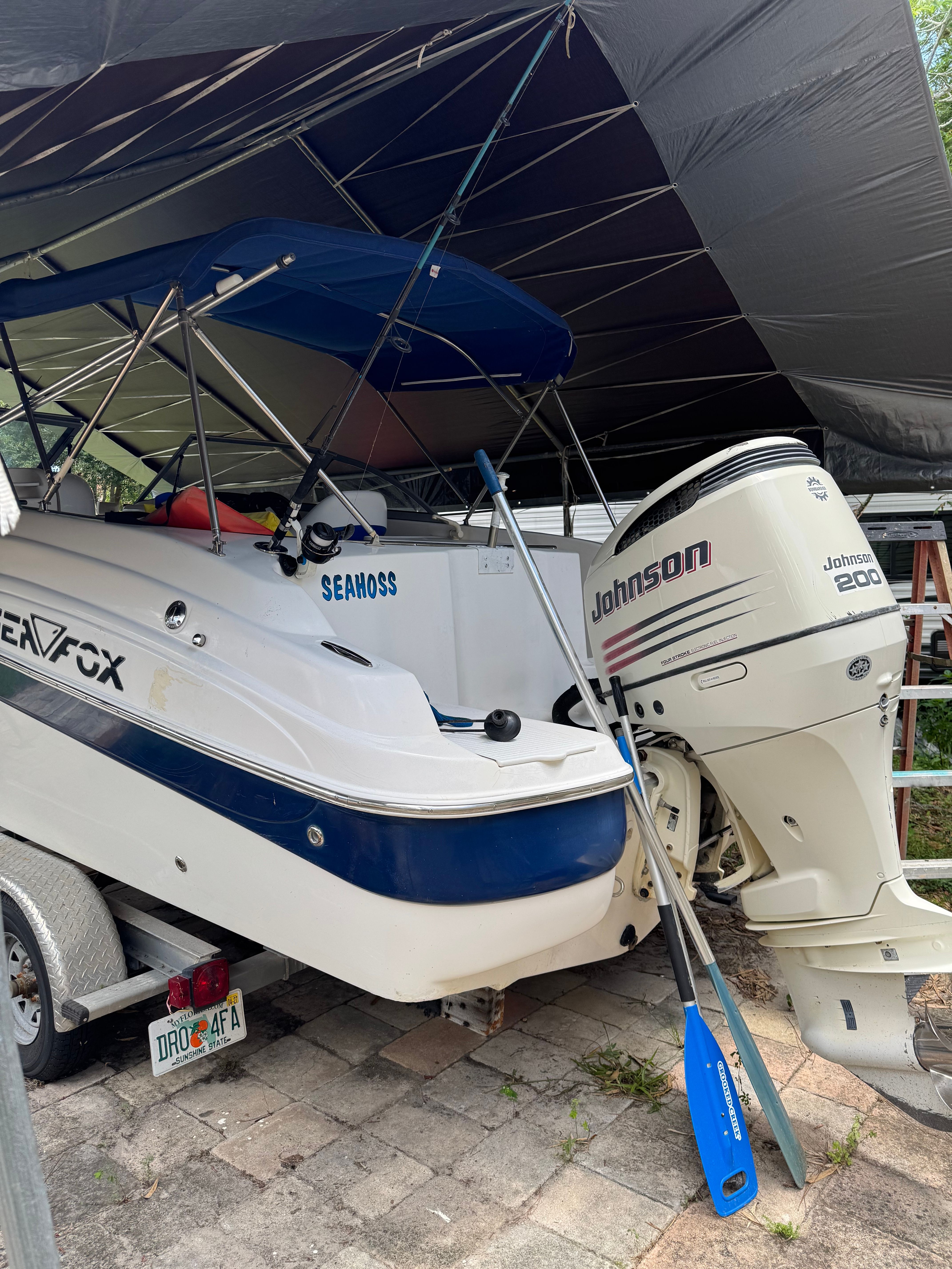 A white boat with a blue stripe sits on a trailer under a shelter.