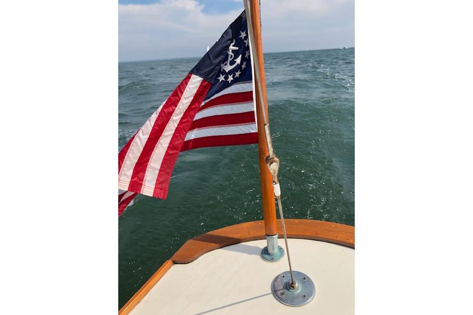 Sailboat with American flag on Cape Cod Shipbuilding Shields, 1963, sailing on open water.