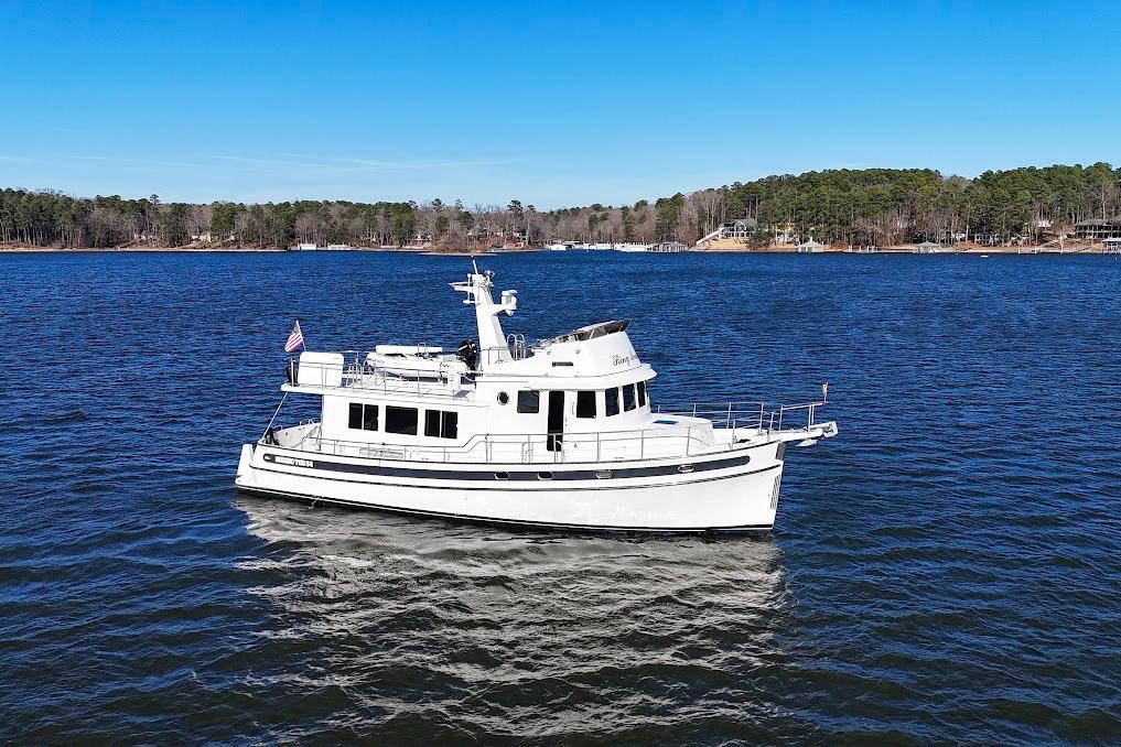 2007 Nordic Tug 54 cruising on a serene lake with forested shoreline.